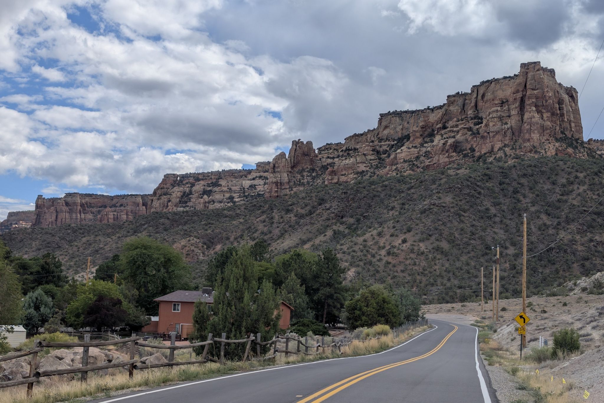 A winding road passes a house, leading towards massive rock formations under cloudy skies. - Colorado Riverfront Trail Loop