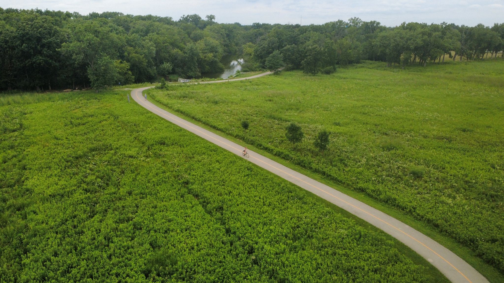 Aerial view of a winding paved path through green fields and forest. - Salt Creek Greenway Trail