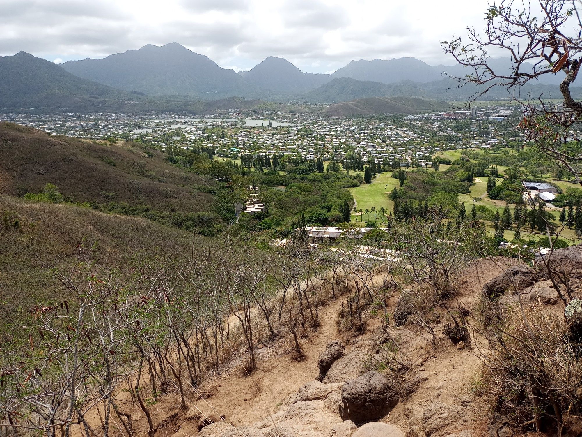 Overlook of a town and golf course with mountains under cloudy skies. - Lanikai Pillbox No. 2 Viewpoint – Lanikai Pillbox 1 loop from Lanikai