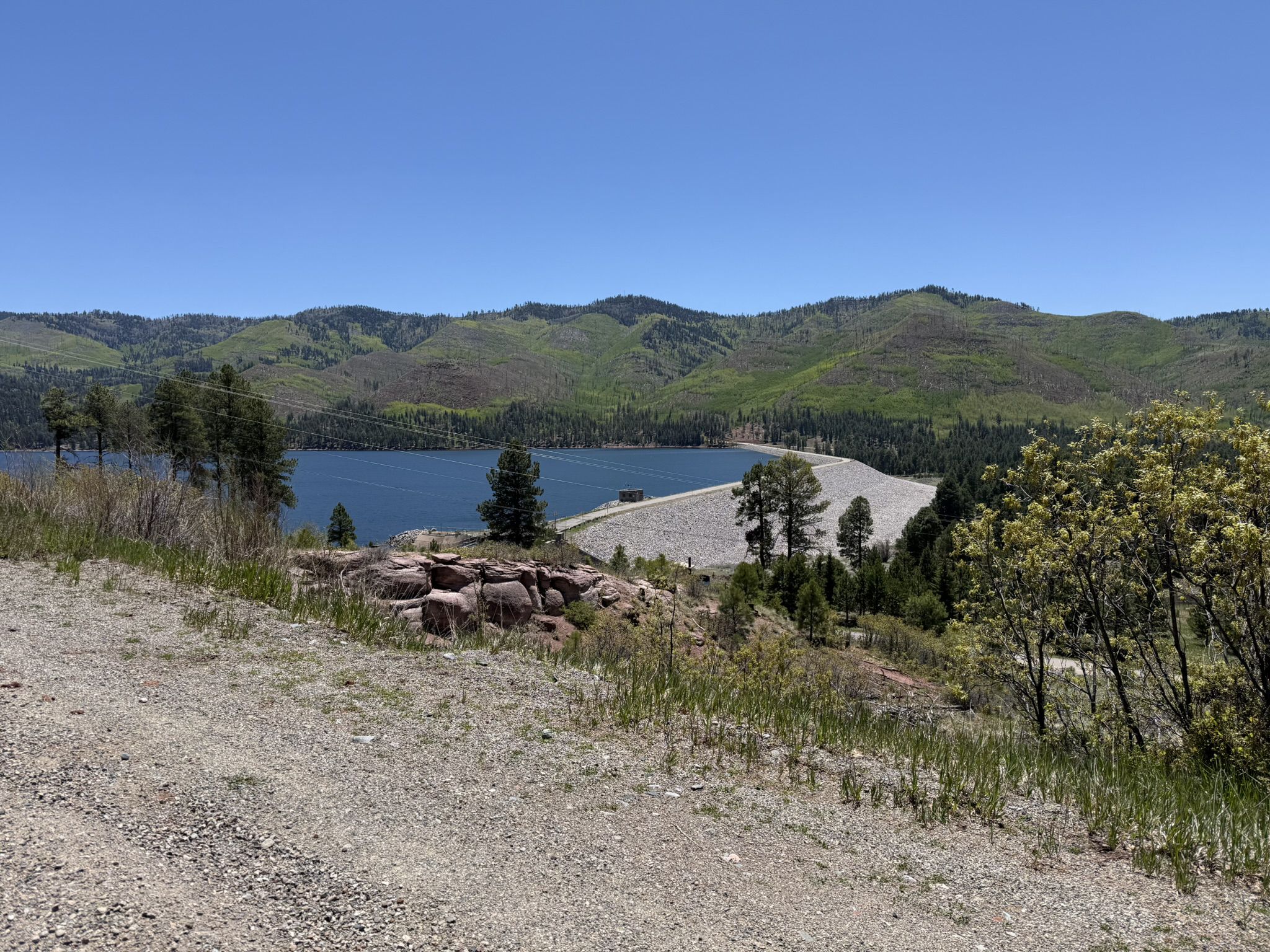 Sunny view of a large lake, dam, and green forested mountains. - Vallecito Reservoir loop gravel