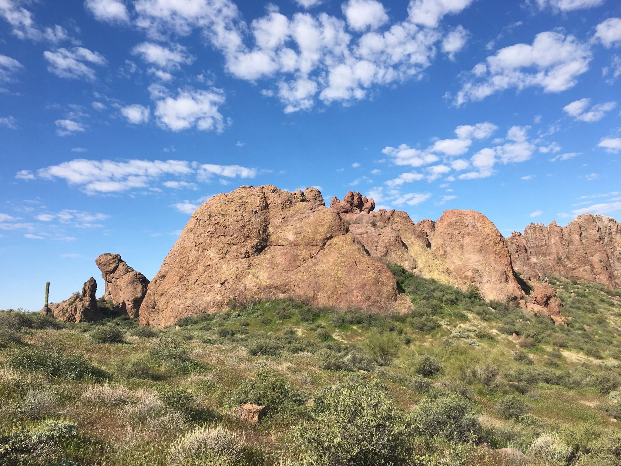 Large reddish-brown rock formations on a green hill under a cloudy blue sky. - Jacob's Crosscut, Prospector's View and Treasure Loop Trail