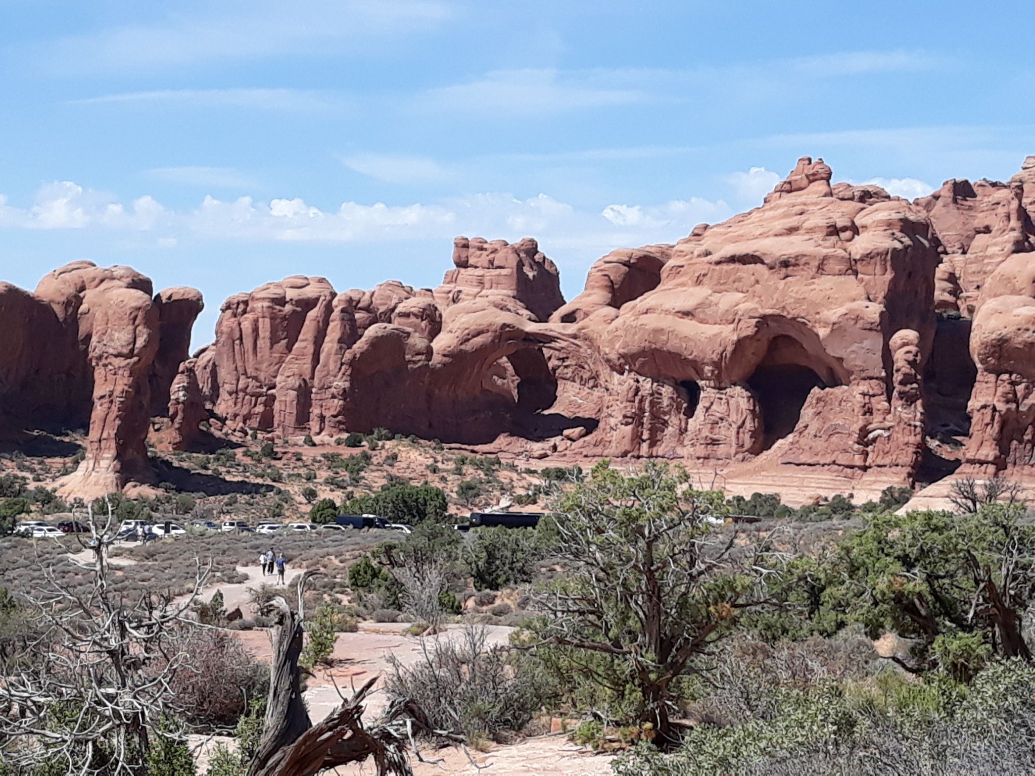 Distant red rock formations and arches in a sunny desert, with people. - North Window Arch – Turret Arch loop from Double Arch