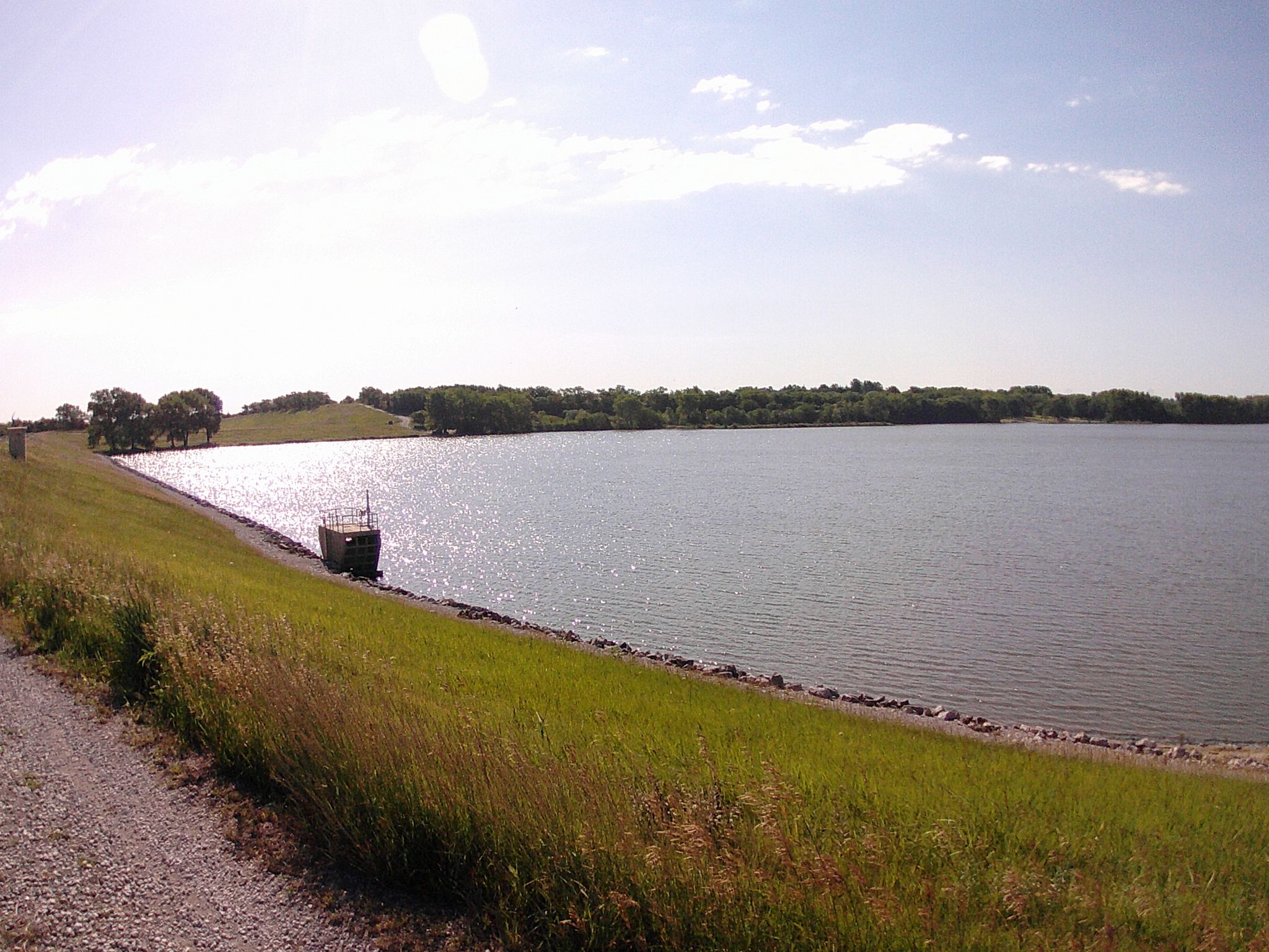 Sunny lake view with a grassy bank and a small structure near the water. - South Rock Island Trail – Pioneers Park loop from The Ridge