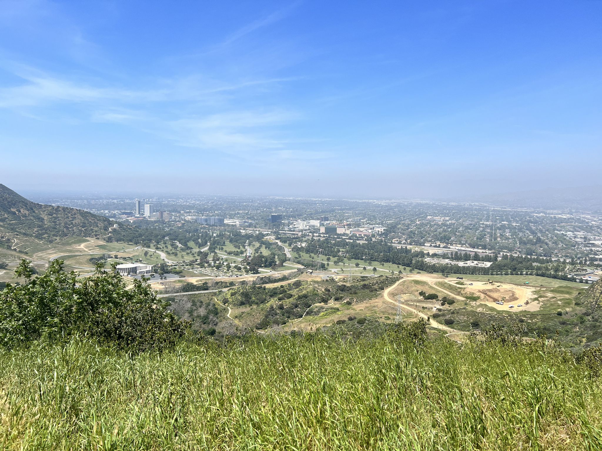 A panoramic view of a distant city and valley from a grassy hilltop. - Red Car Bridge – Baum Bicycle Bridge loop from Atlantic