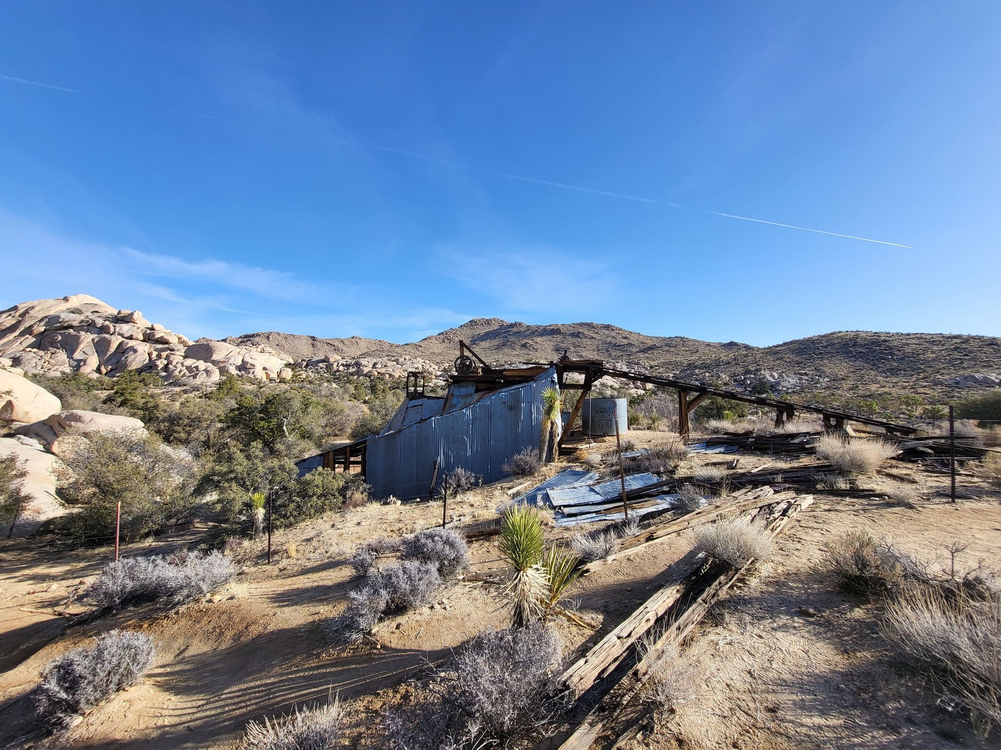 Abandoned corrugated metal mining structure on a sunny desert hillside with clear sky. - Wall Street Mill Trail