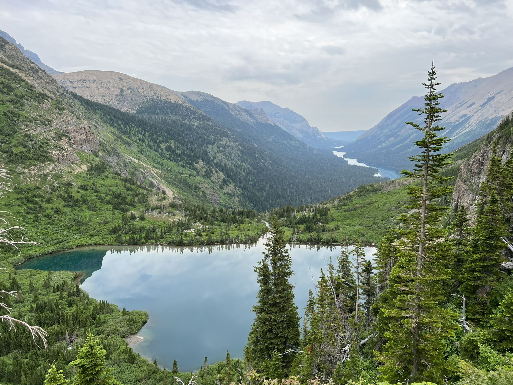 Overcast view of a serene blue mountain lake surrounded by lush green slopes. - Belly River Trail