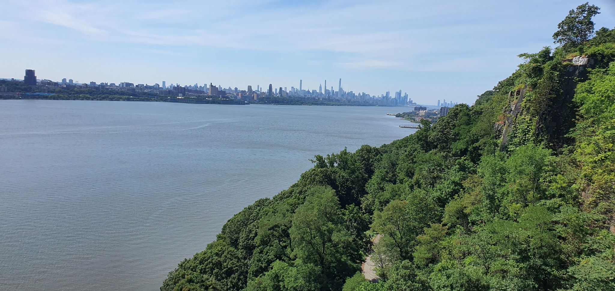 Wide river flowing past a green forested cliff under a clear sky. - Palisades loop over the Hudson