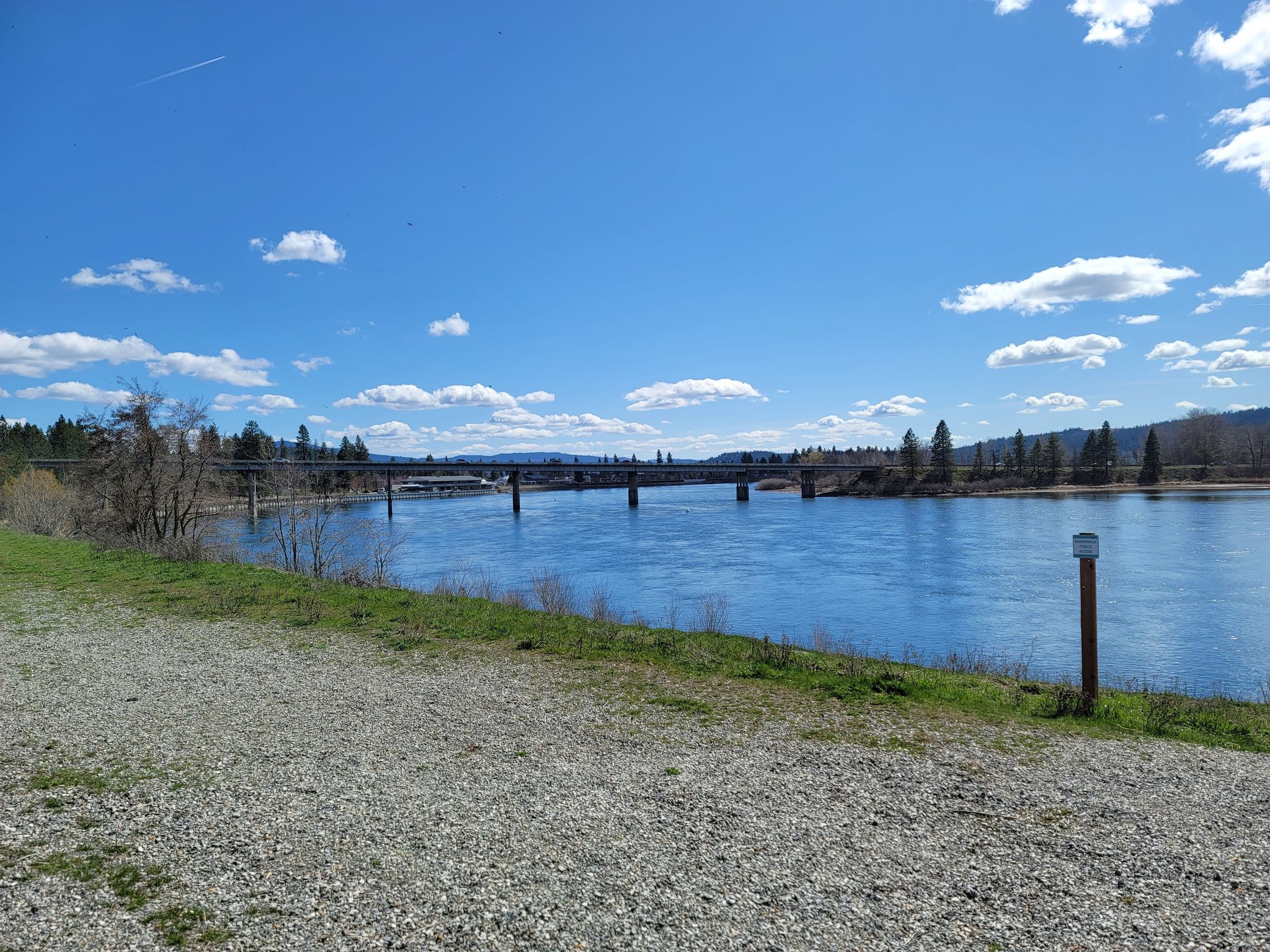 A long bridge spans a wide blue river with green banks under a bright sky. - North Idaho Centennial Trail