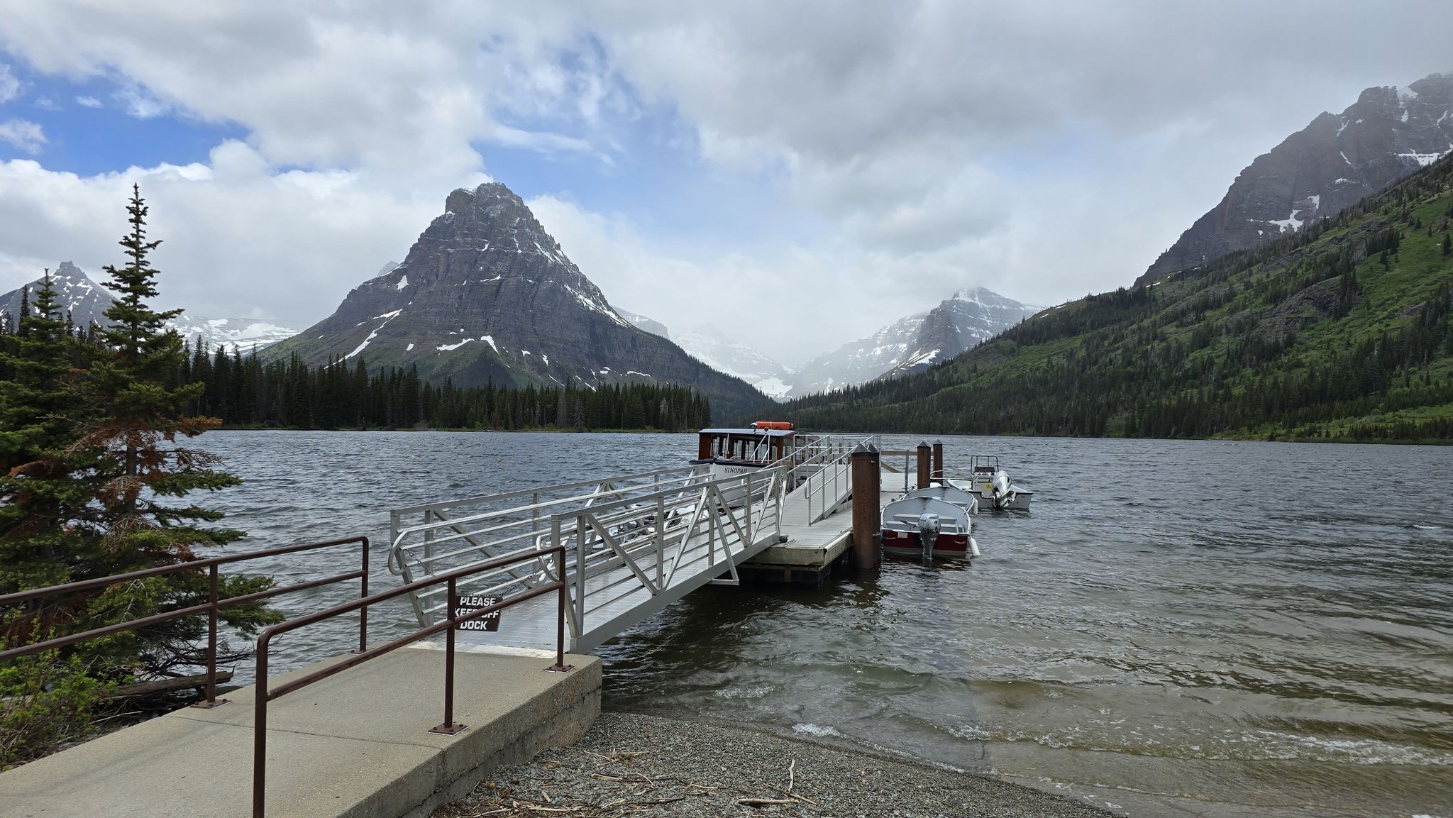 A boat dock extends into a lake with majestic snow-capped mountains under cloudy skies. - Aster Falls