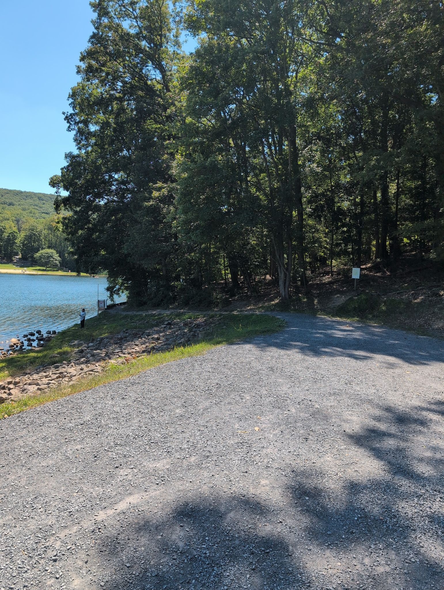 Gravel path next to a lake shore, surrounded by dense green trees. - Big Red Trail