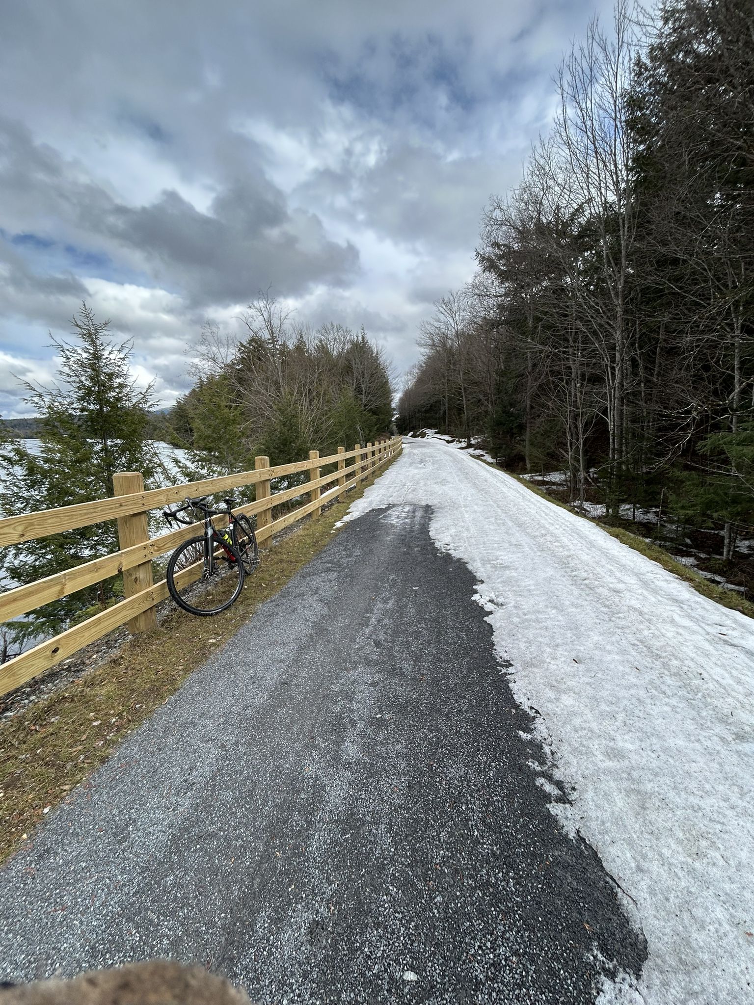 Bicycle parked beside a wooden fence on a snowy path under cloudy skies. - Adirondack Rail Trail