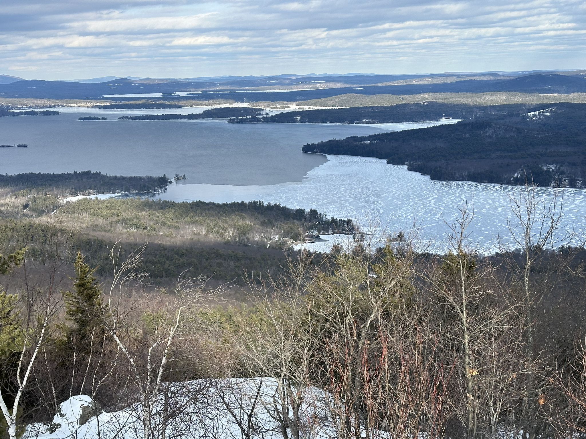 Overcast aerial view of a partially frozen lake surrounded by forested hills. - Mount Major Trail