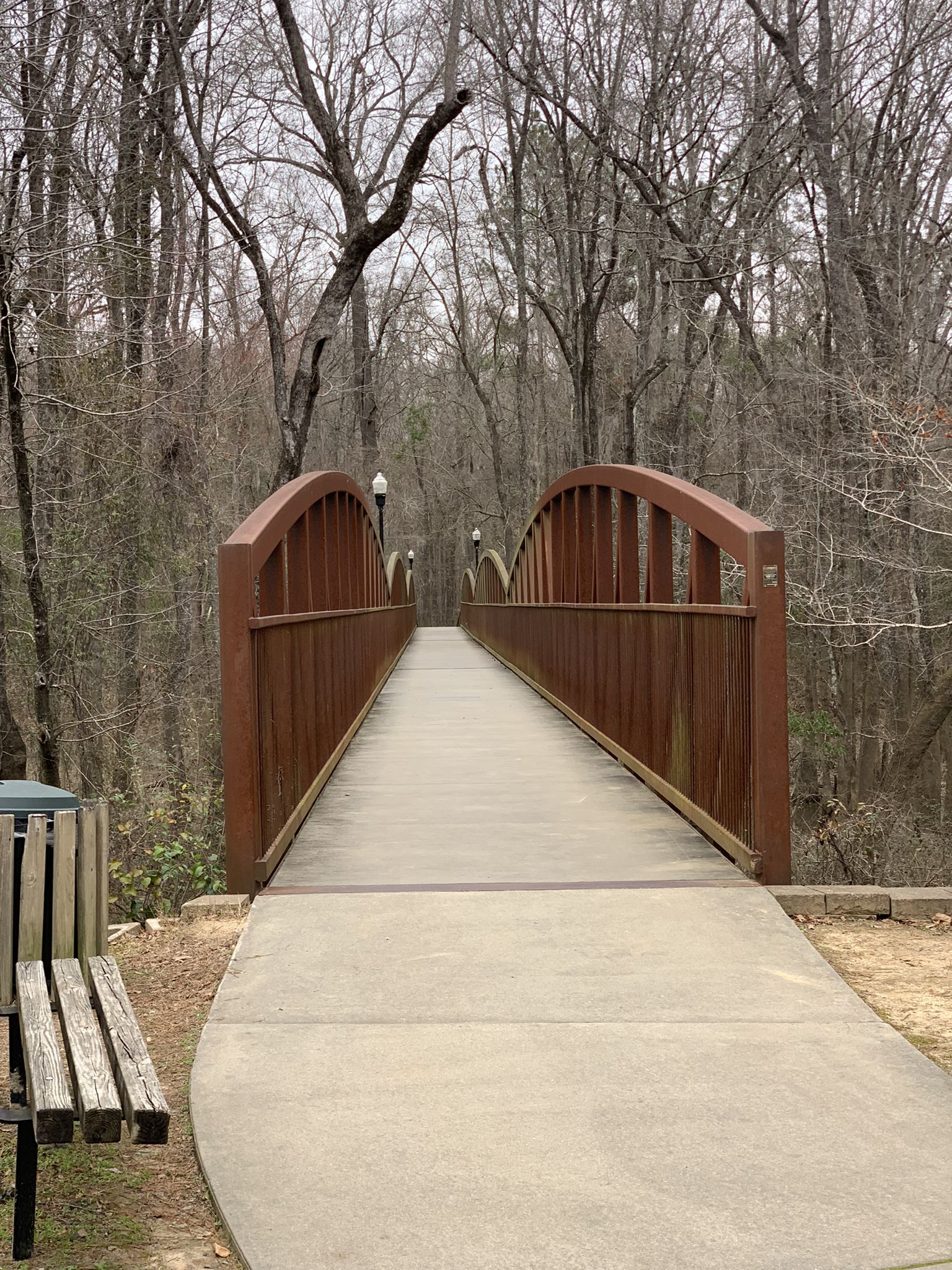 Concrete path leading to an arched wooden bridge through bare trees. - Timmerman Trail