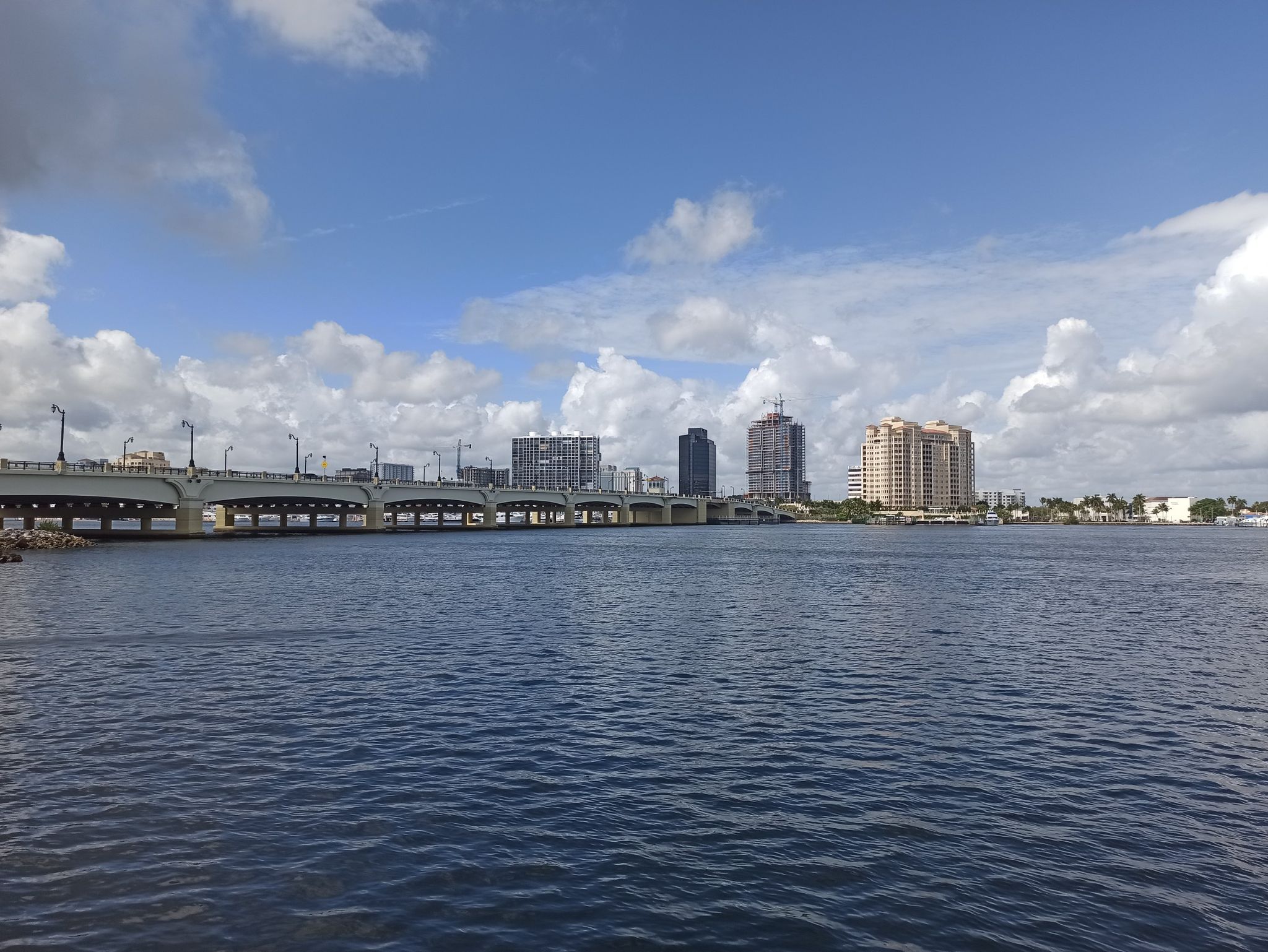 Wide river with a long bridge and city skyline under a cloudy blue sky. - Lake Trail – Lake Trail loop from West Palm Beach