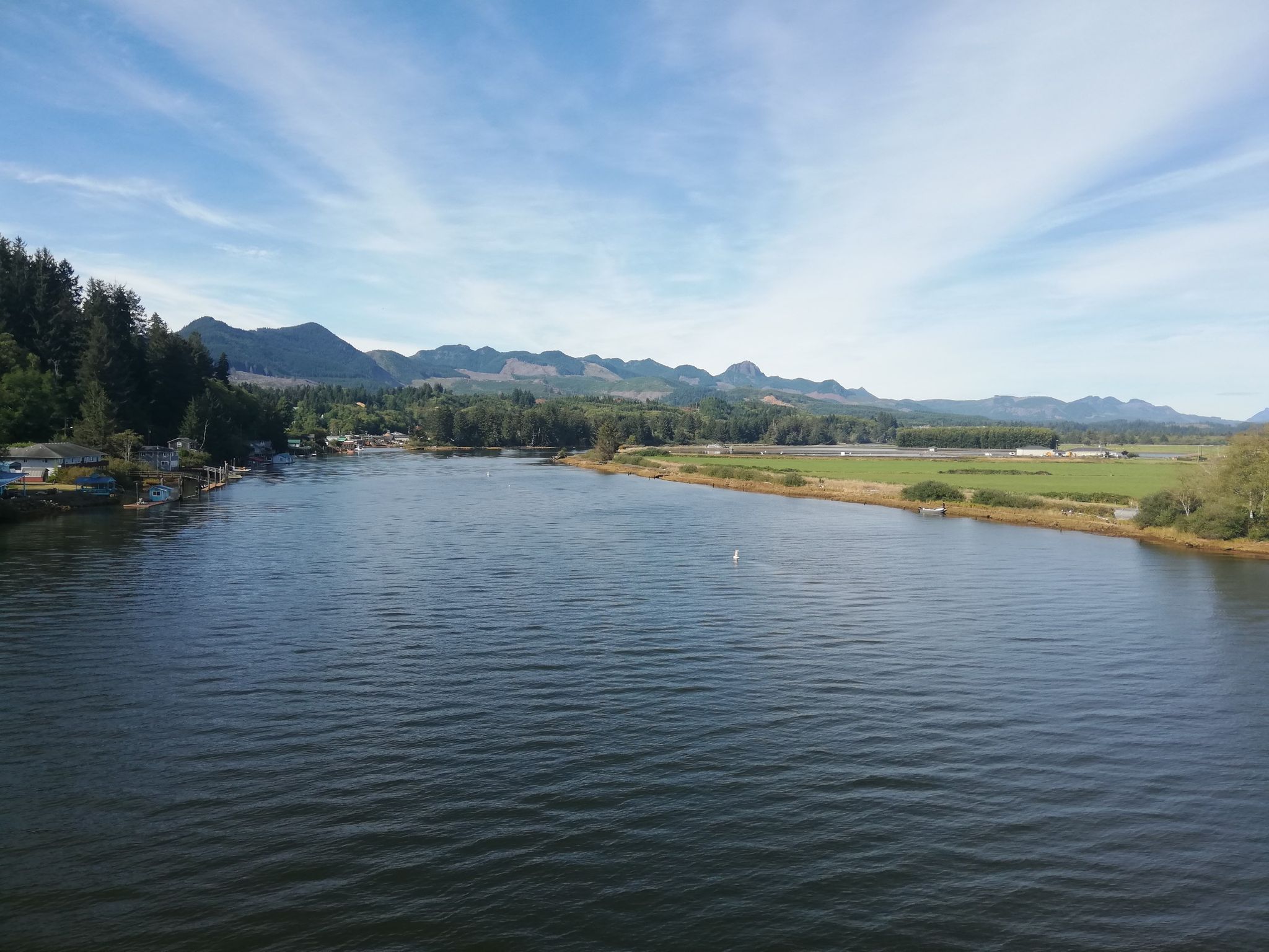 Wide river with forested banks, distant mountains, and a partly cloudy blue sky. - Nehalem River loop