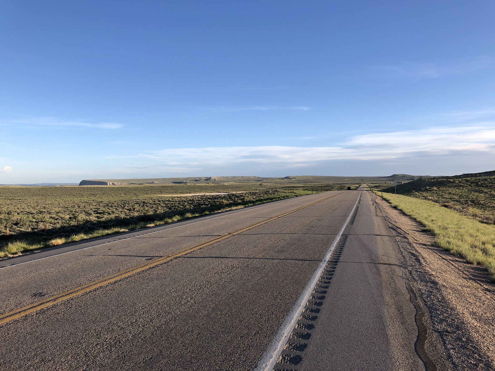 An empty, straight road extends through a vast, sunny, arid landscape. - TransAmerica Trail: Rawlins to Saratoga