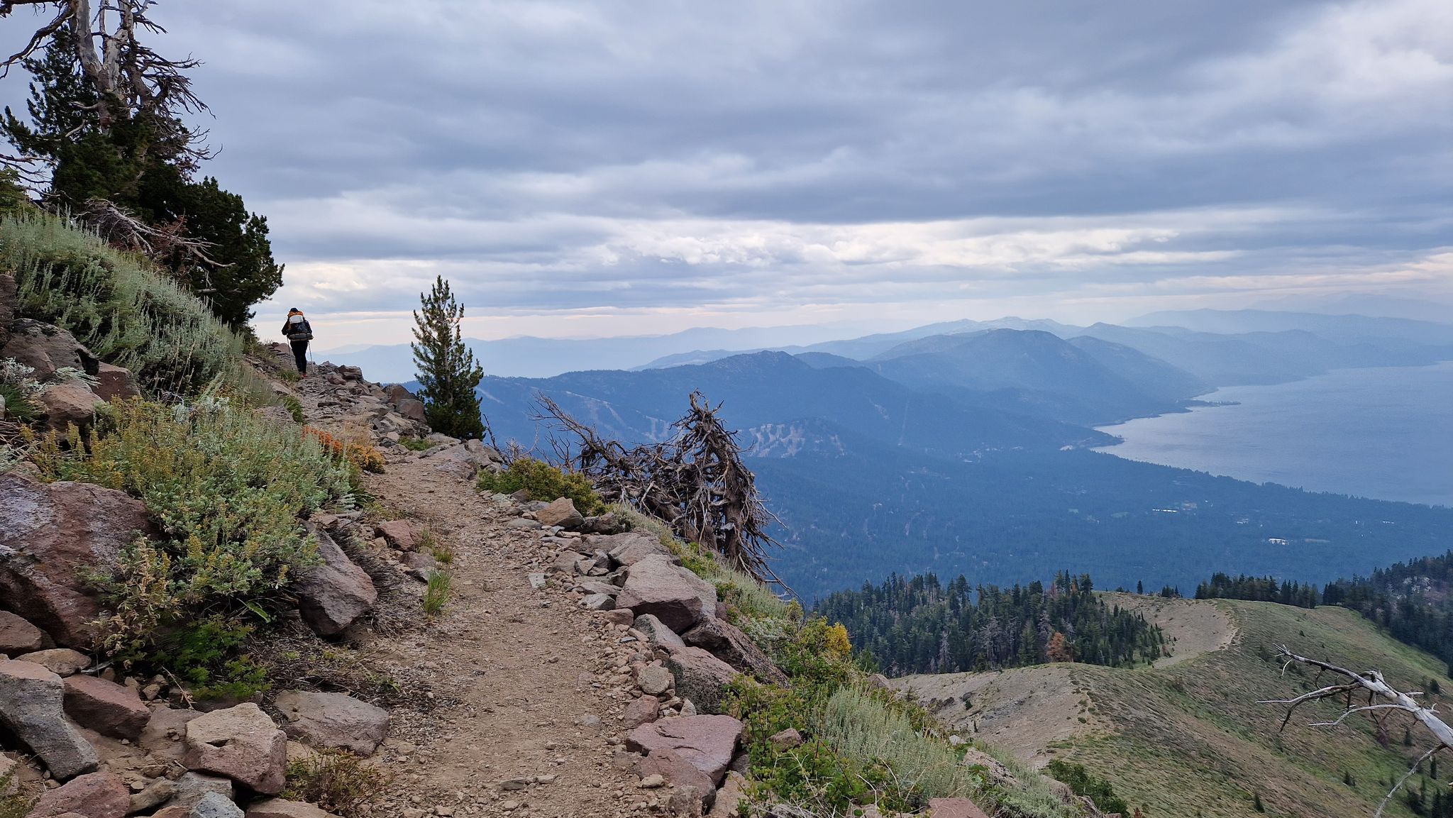 Hiker on a rocky mountain trail overlooking a large lake under cloudy skies. - Tahoe Rim Trail: Brockway Summit to Mount Rose Summit