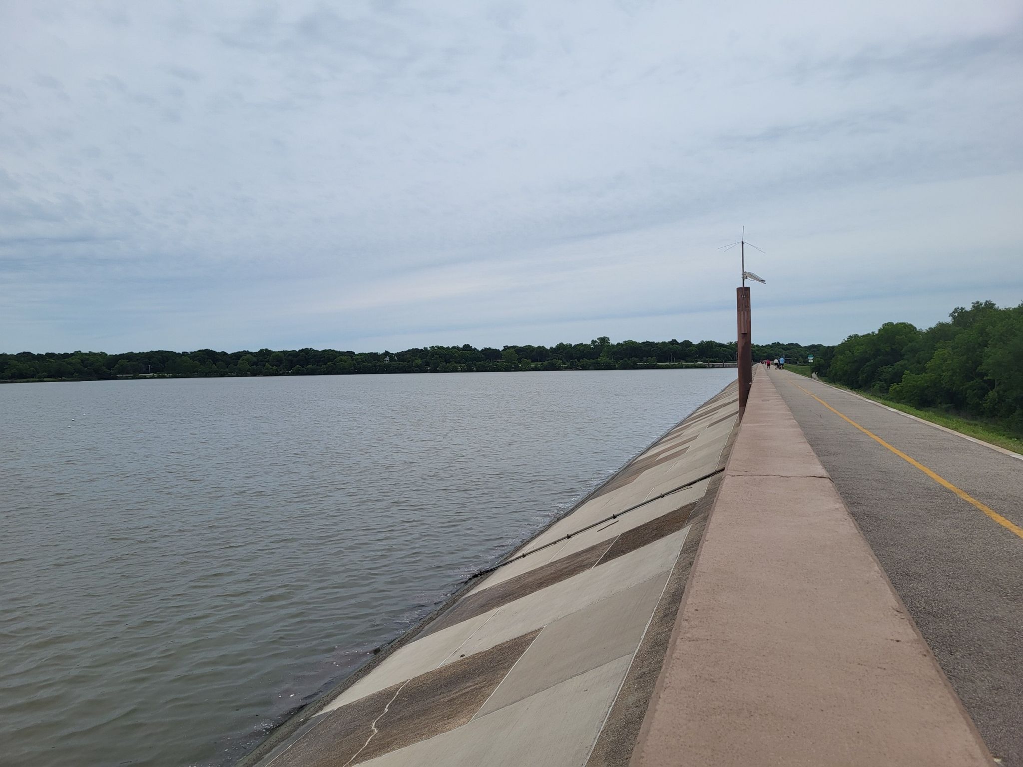 Concrete embankment and road beside a wide, calm body of water. - White Rock Lake Dam – White Rock Lake Spillway loop from SMU/Mockingbird