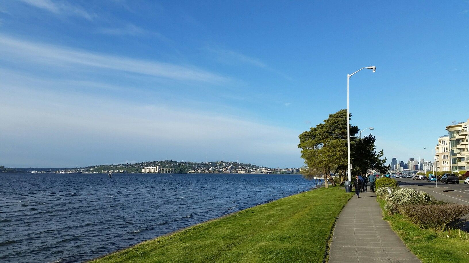 People walk on a paved path beside a large body of water. - Alki Trail – Seacrest Park loop from Tukwila International Boulevard