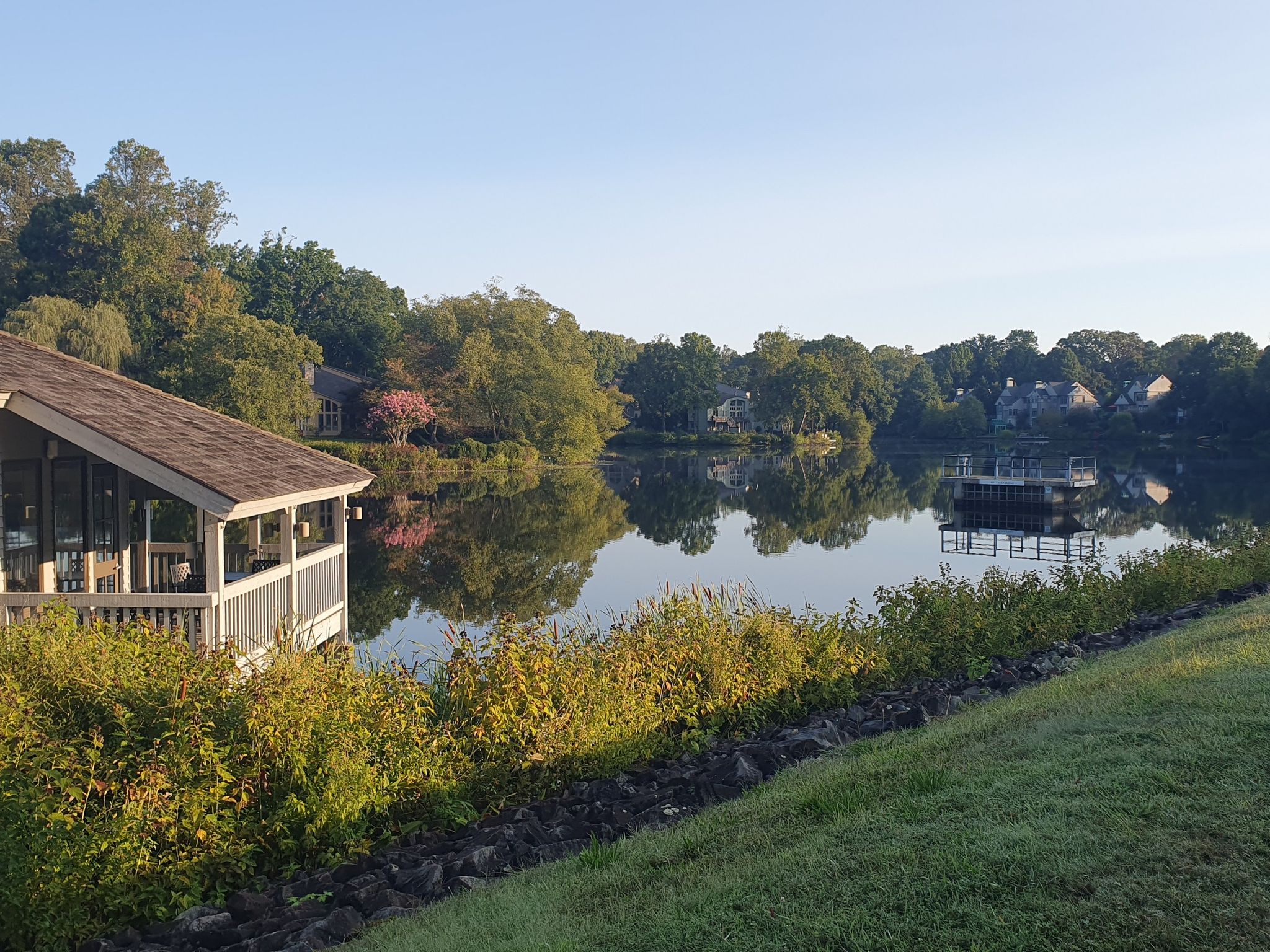 Lakeside boathouse and dock with reflections of trees and distant houses. - Baron Cameron Park Loop