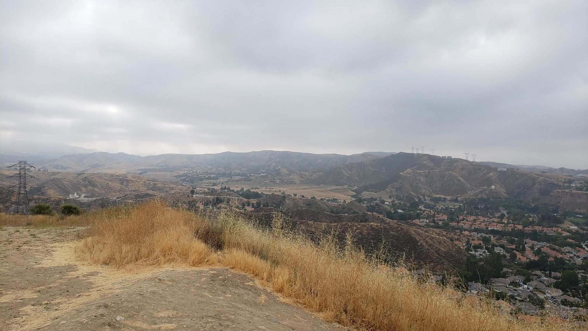 Overcast view of dry hills, valleys with homes, and power lines from a dirt path. - Haskell Canyon Open Space