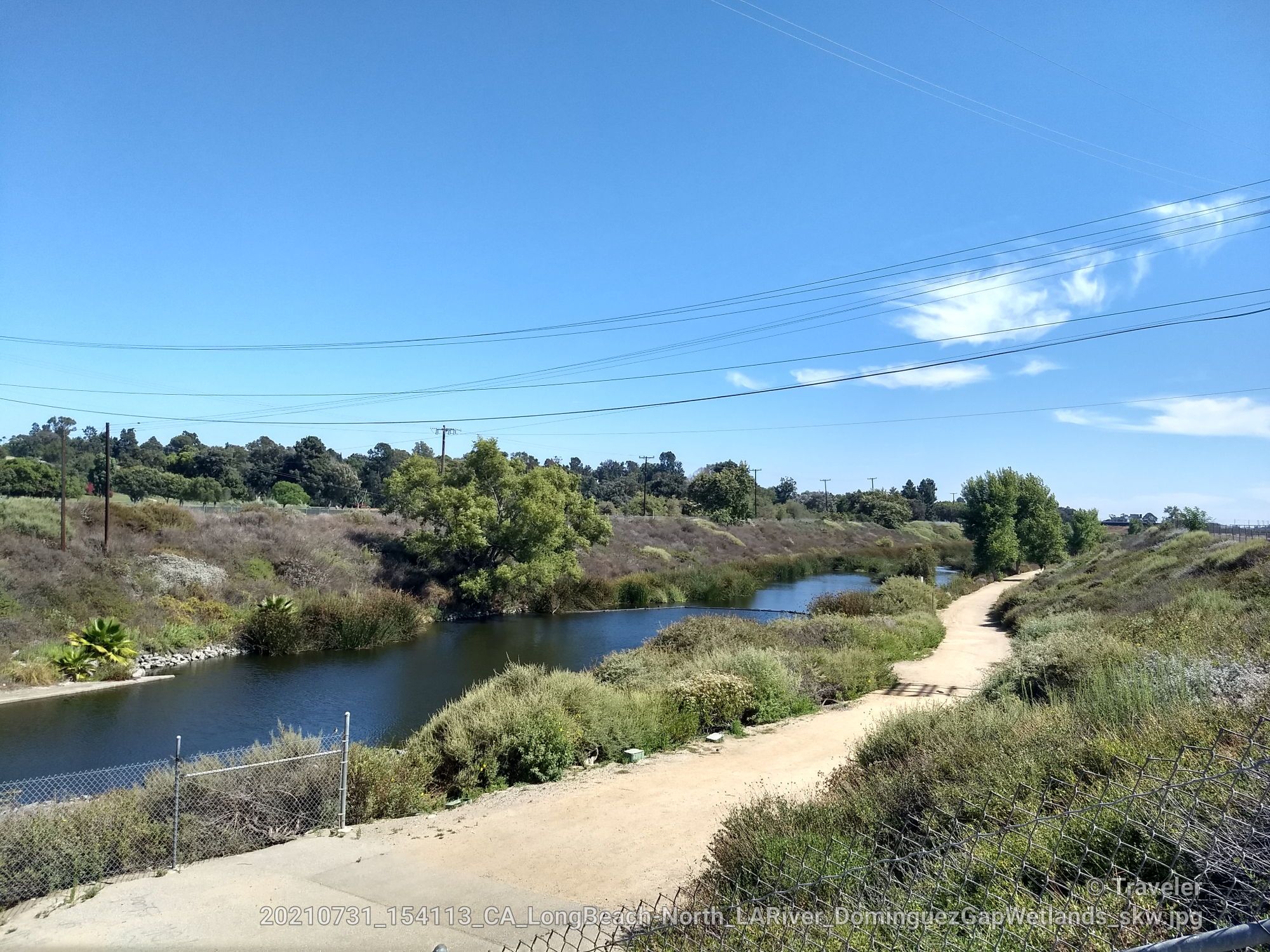 Sunny dirt path alongside a calm river with green reeds and distant trees. - Beautiful Beach Bike Path – Long Beach City Beach loop from Del Amo