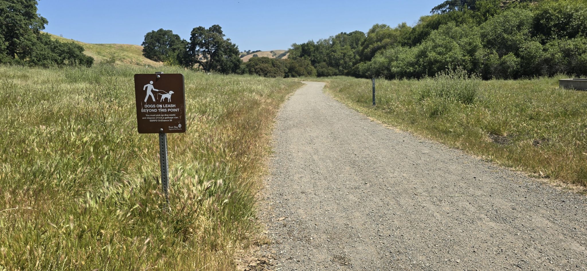 A dog-on-leash sign stands beside a dirt path through sunny fields. - Diablo View and Alhambra Creek Trail Loop
