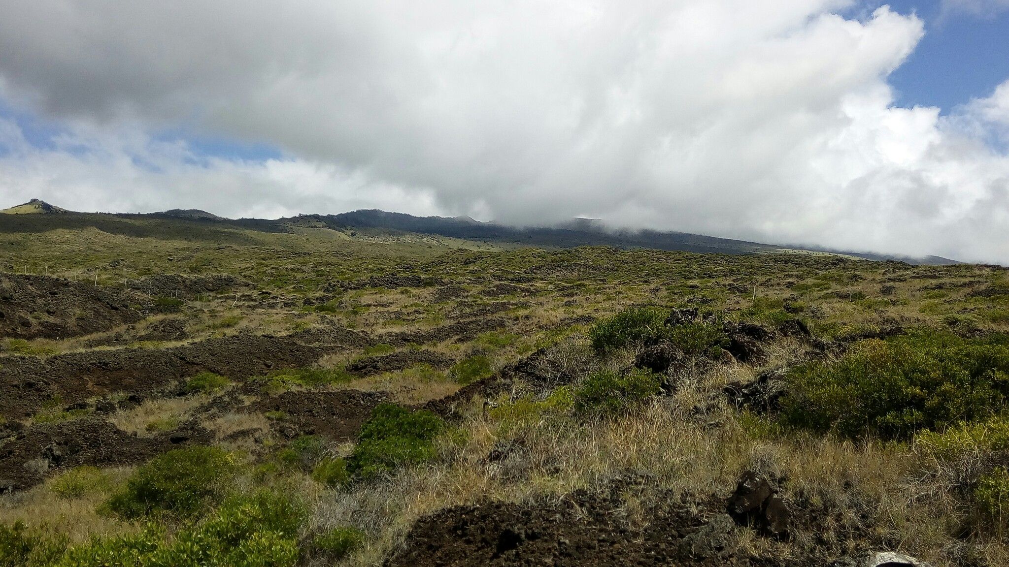 Expansive rocky, grassy landscape under a partly cloudy sky with distant mountains. - Kepuni Rocks Viewpoint loop from Keokea