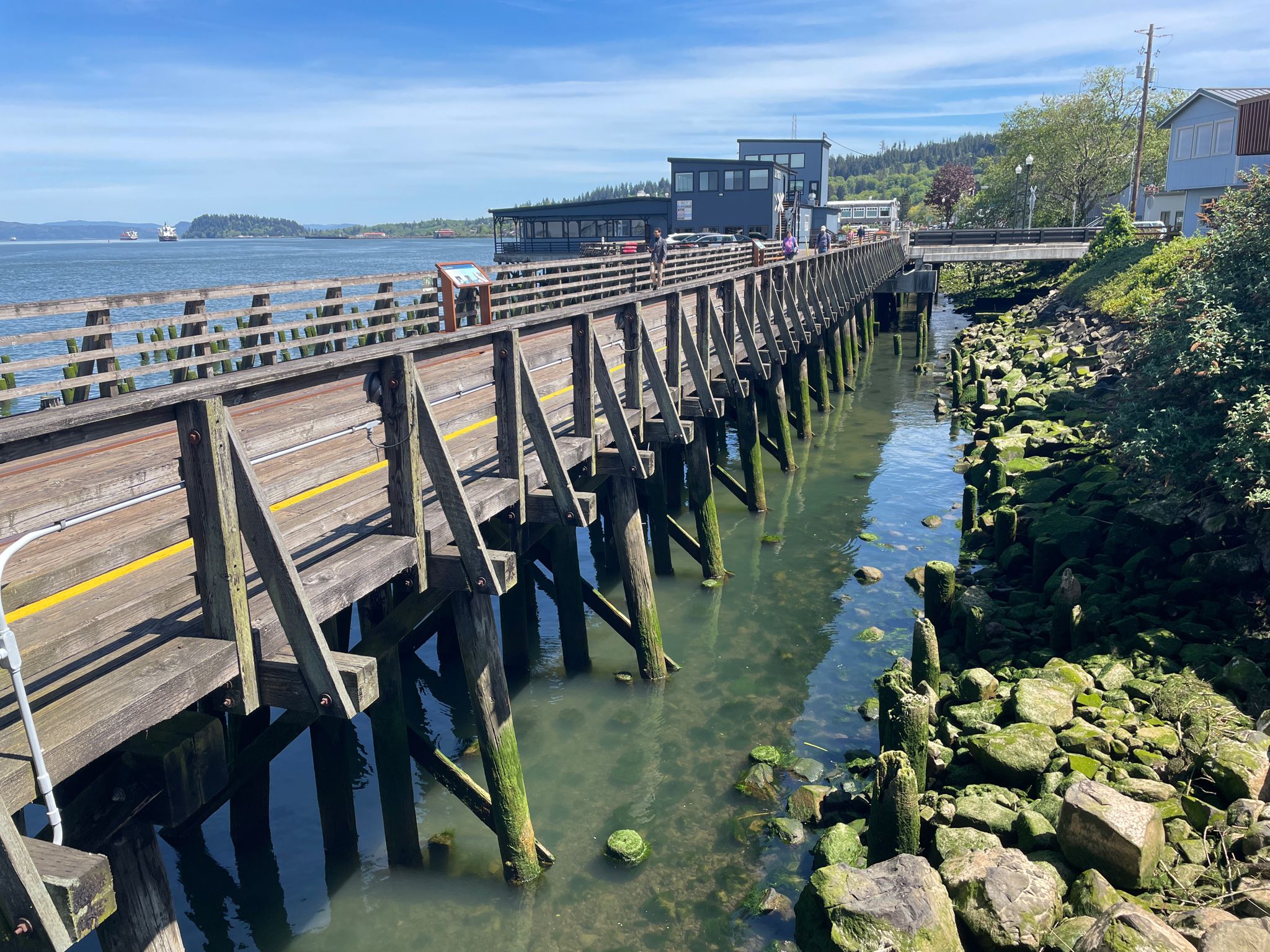 Long wooden pier over calm water, buildings on shore, bright sunny day. - Astoria–Megler Bridge loop from Astoria