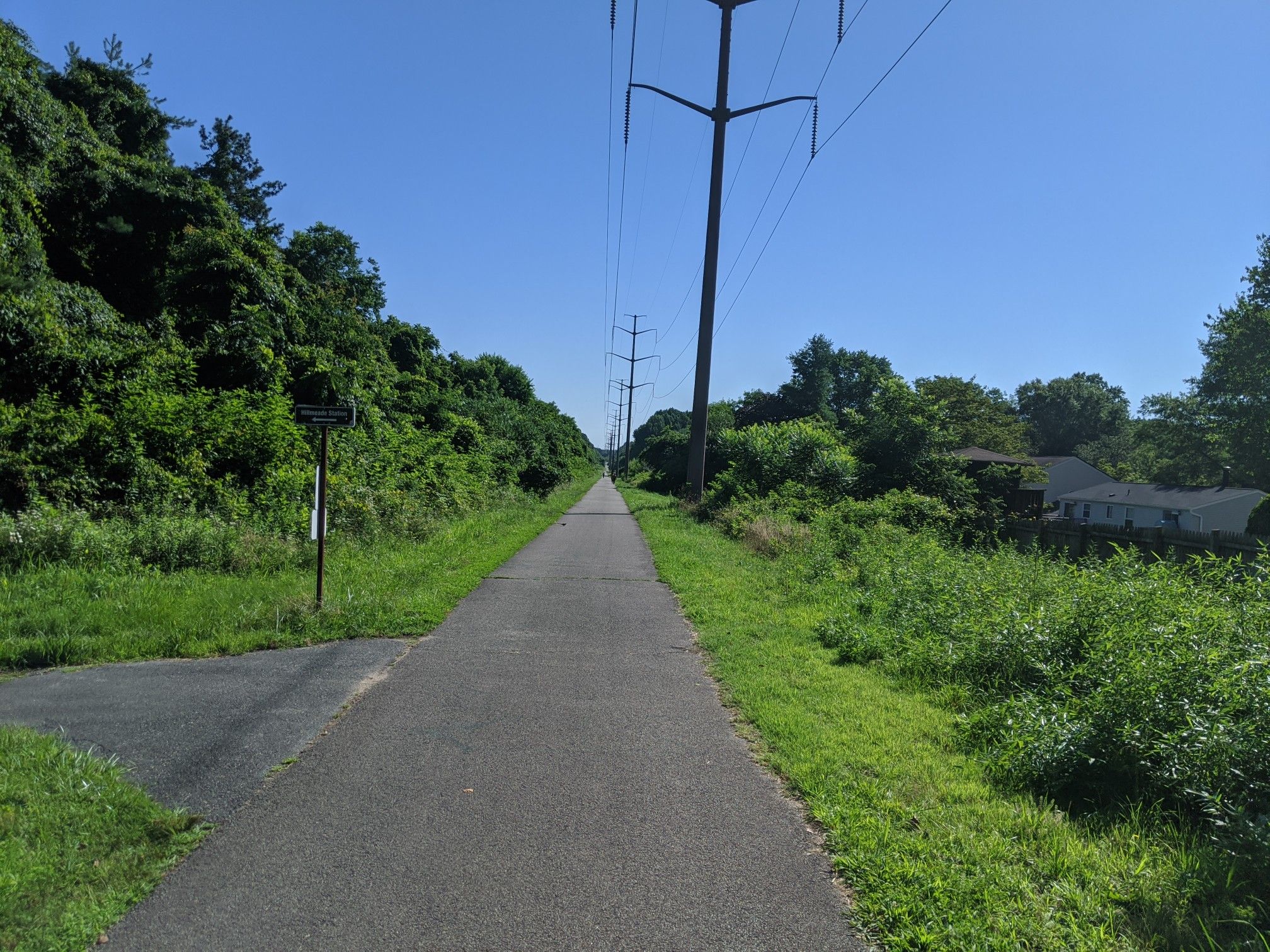 Paved path stretching into distance, flanked by lush green trees under bright sky. - WB&A and East Coast Greenway Loop from Odenton