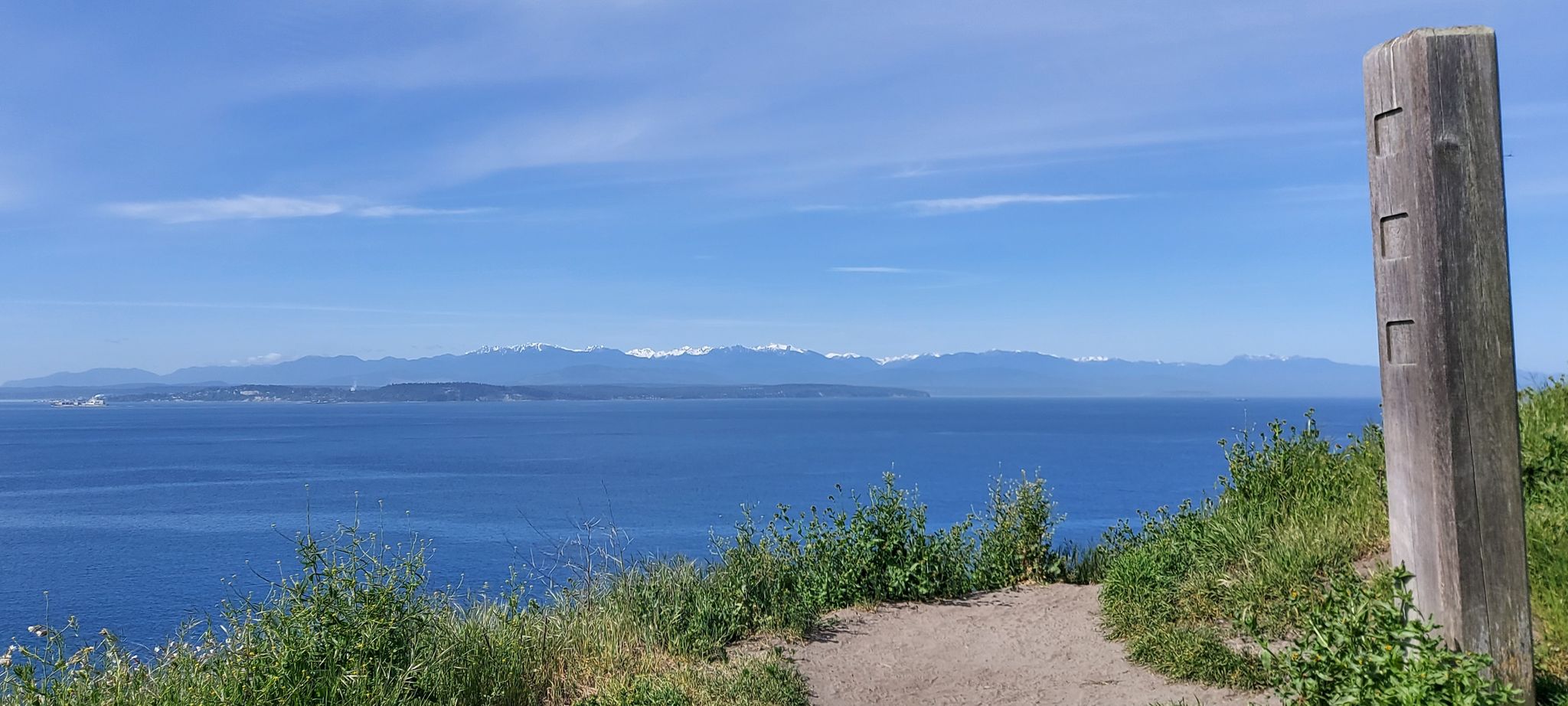 Dirt path on a grassy bluff overlooking a blue sea and distant mountains. - Bluff Overlook loop from Ebey's Landing National Historical Reserve