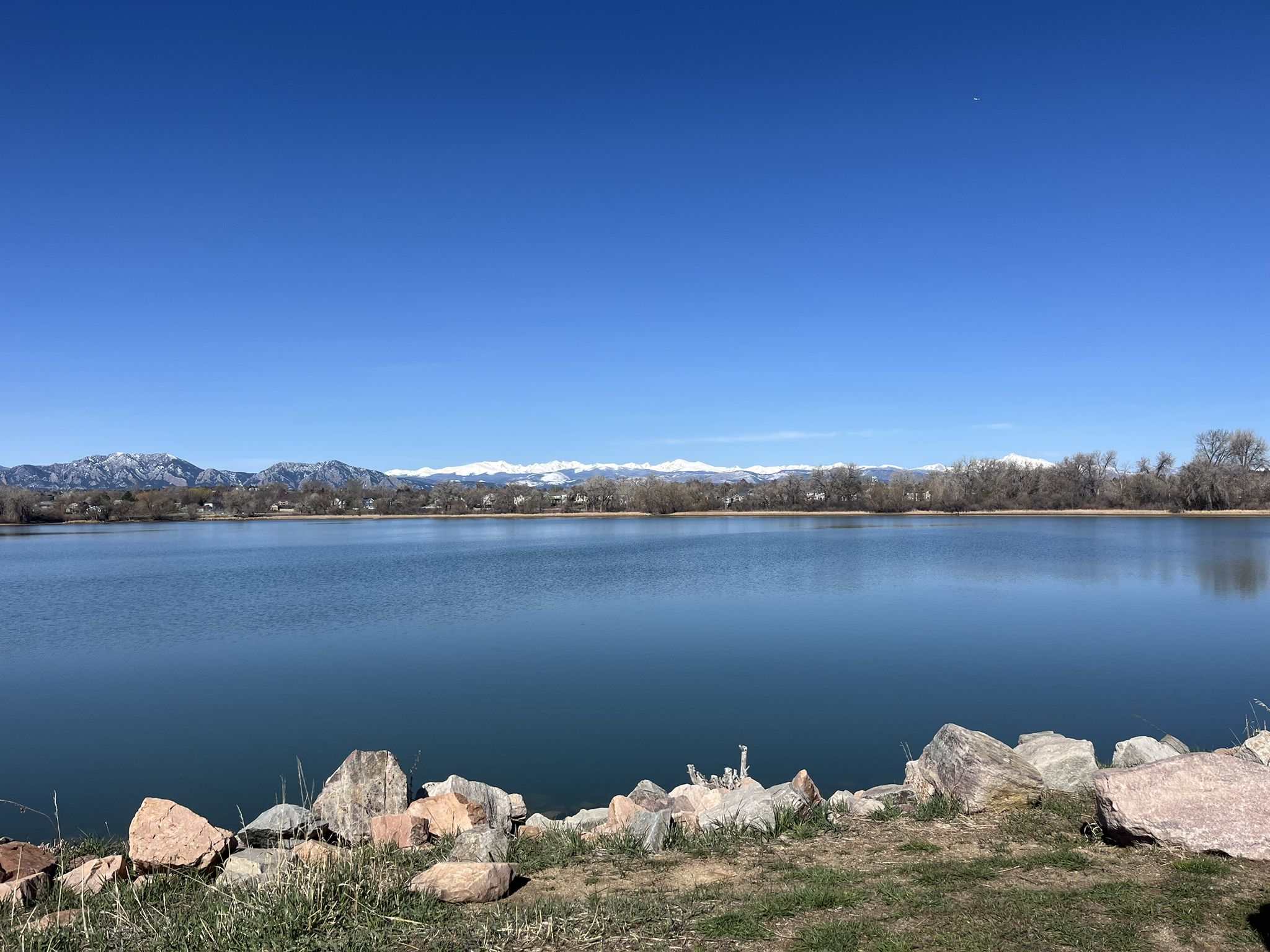 Blue lake with rocky shore, distant snow-capped mountains under clear sky. - Waneka Lake Trail