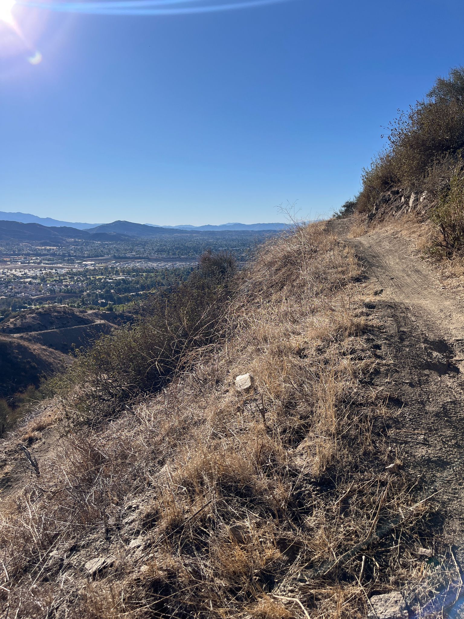 A steep, dry hillside with a narrow path overlooks a distant valley. - Grape Avenue Trail