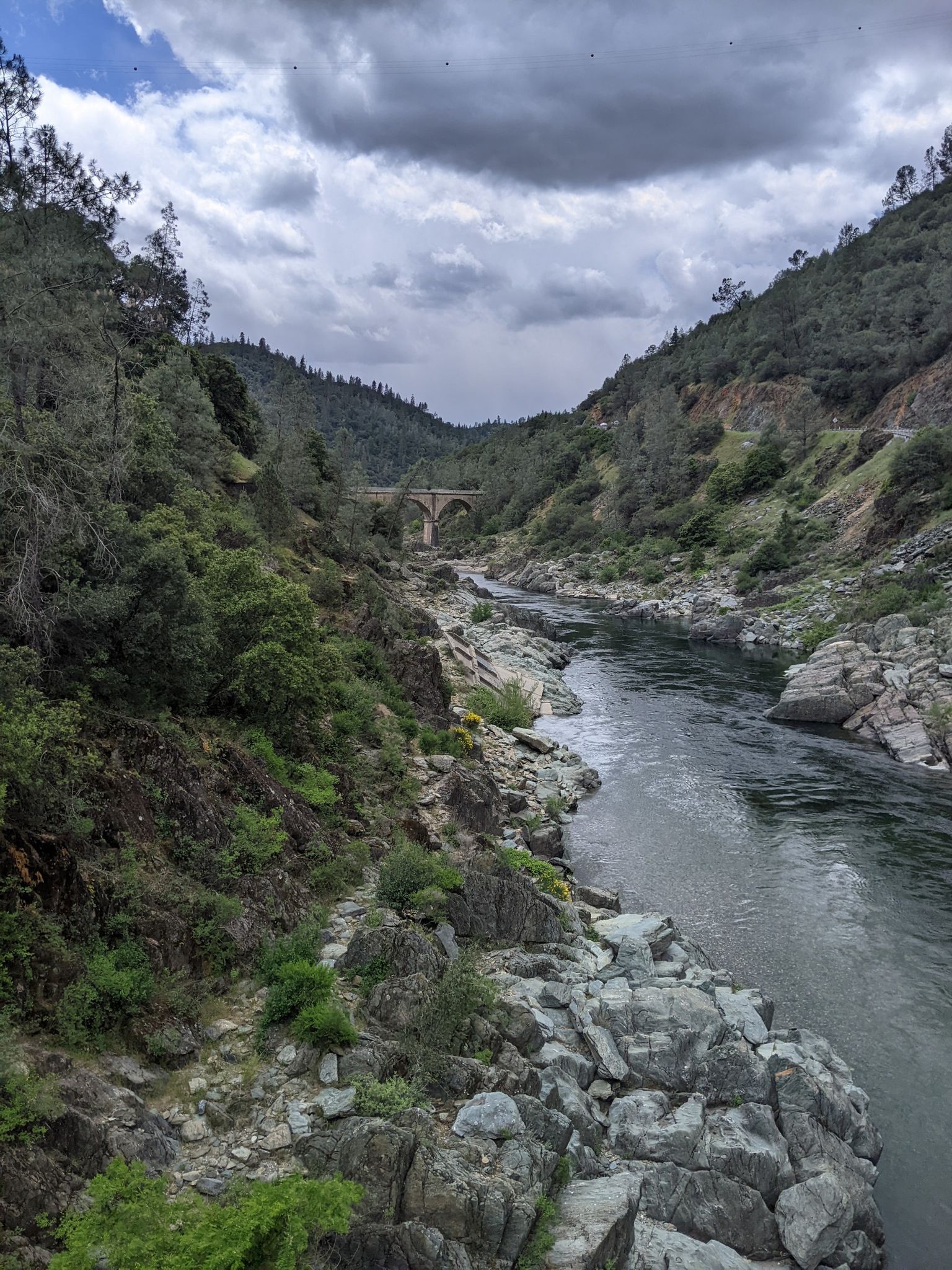 River flows through a rocky canyon under a cloudy sky, with a distant bridge. - Western States 100 Endurance Run