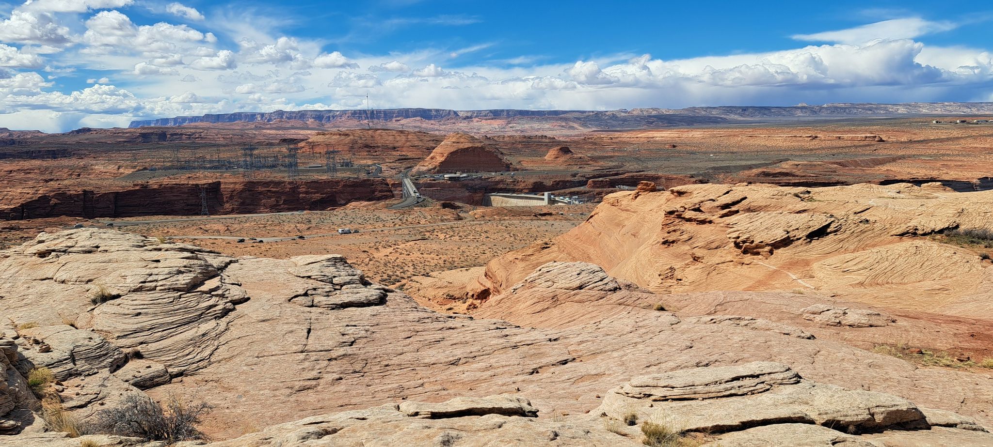 Expansive desert landscape with rocky terrain, distant structures, cloudy sky. - Rimview Trail