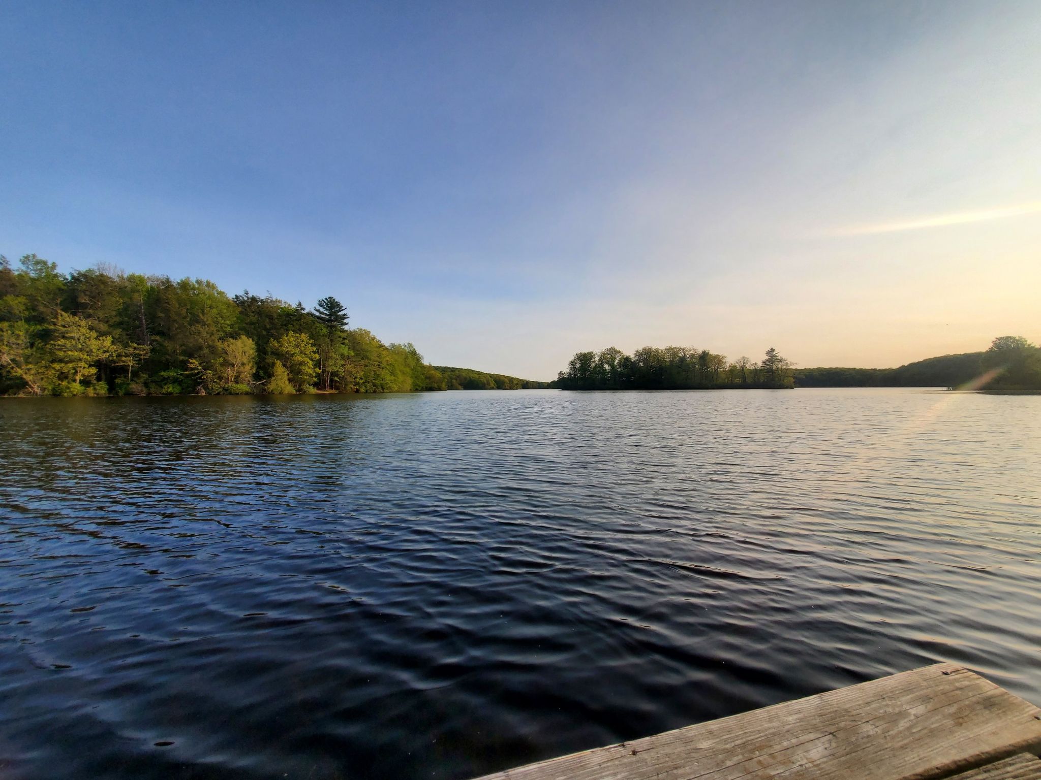 Wide river with forested banks under a clear sky, wooden dock in foreground. - Wawayanda Lake Loop
