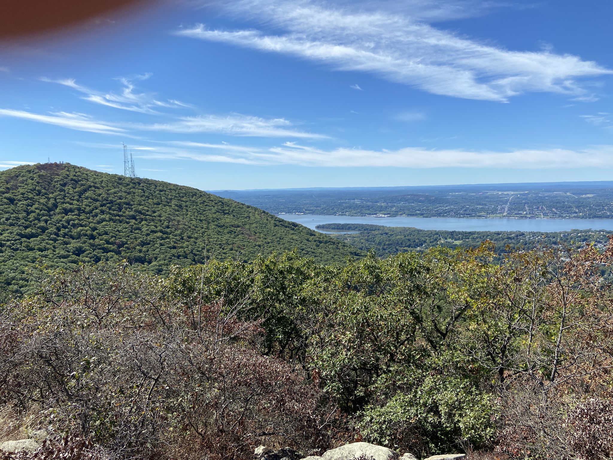 A forested mountain overlooks a wide river under a bright, cloudy sky. - Mount Beacon, Scofield Ridge, and Fishkill Ridge Loop