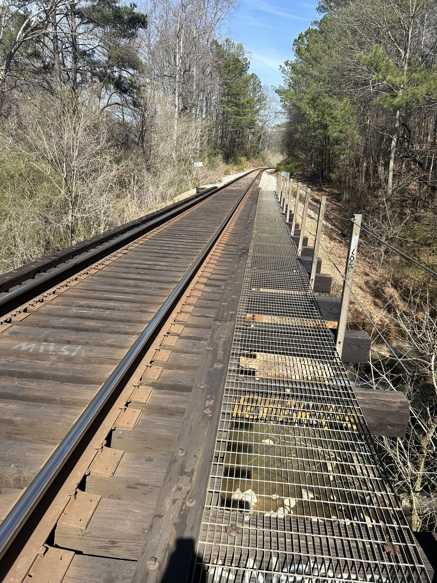 Sunny view of railroad tracks and a grated bridge over water, flanked by trees. - South Peachtree Creek Trail