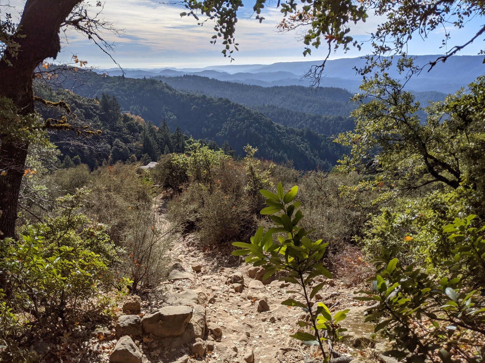 Rocky trail descends into a forested valley under a partly cloudy sky. - Saratoga Gap and Ridge Trail Loop