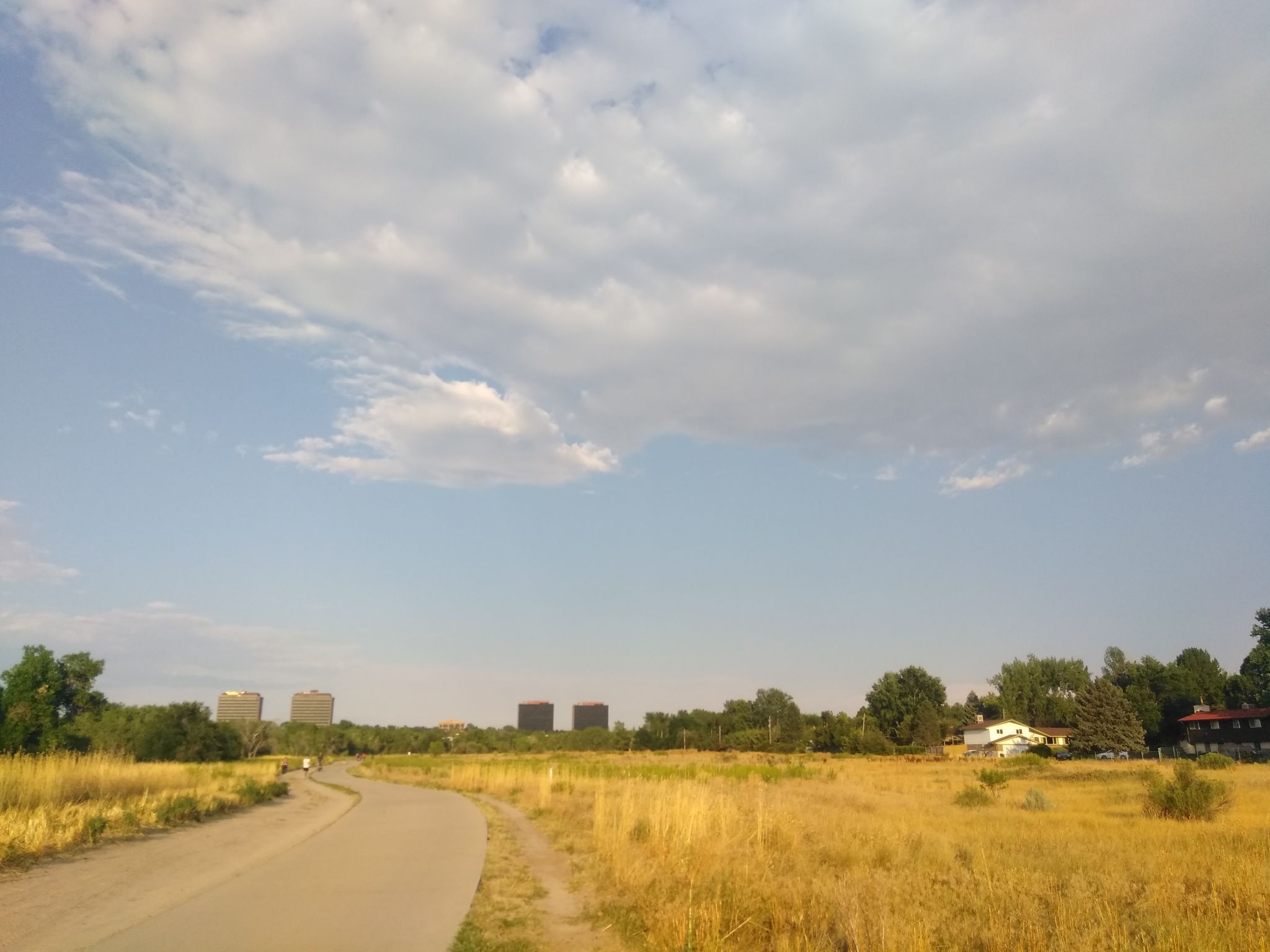 Paved path through golden dry grass, distant buildings under a cloudy sky. - Four Mile Historic Park – Cherry Creek Trail North loop from Glendale