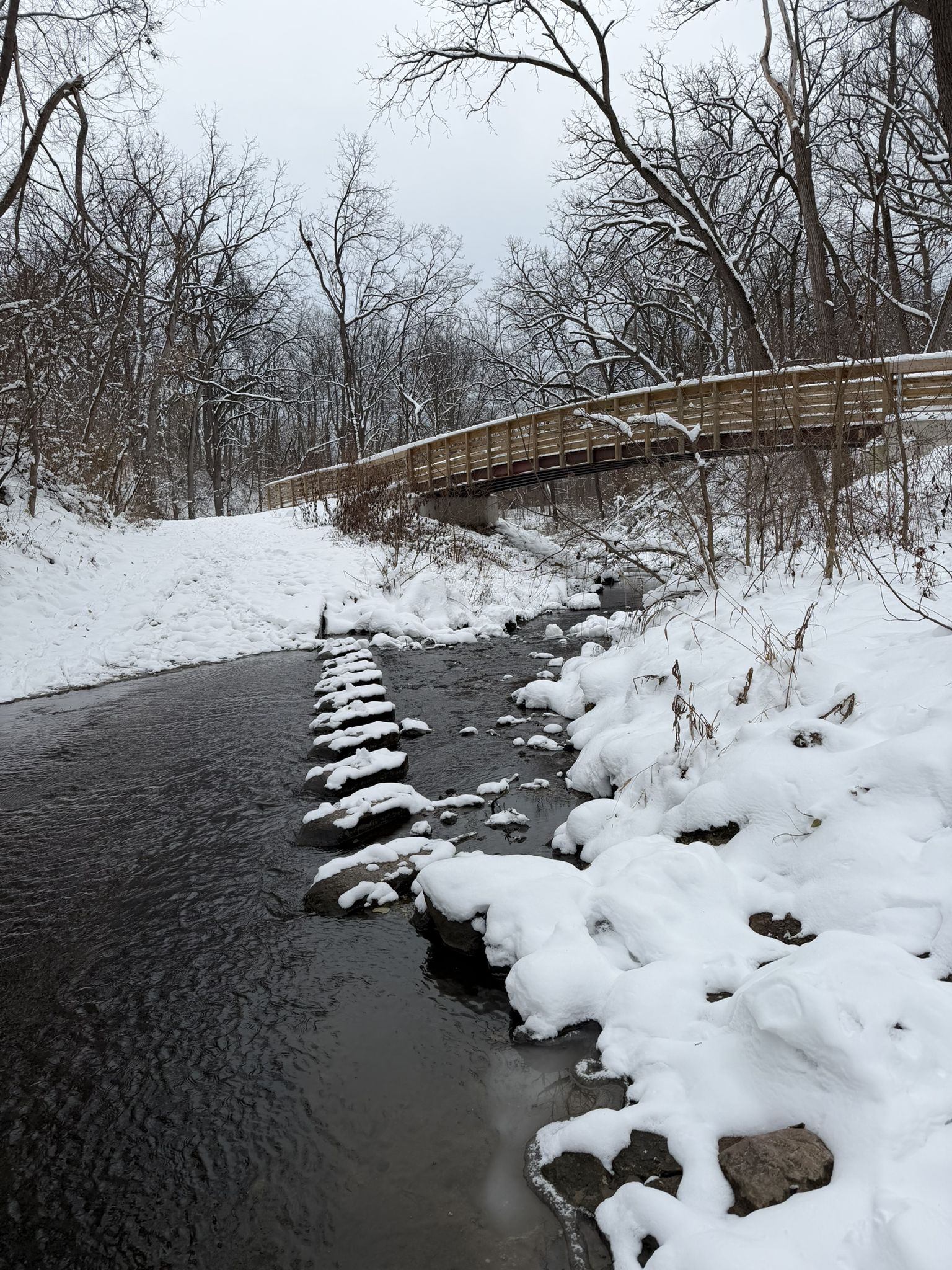 Snow-covered stream with stepping stones and a wooden bridge in winter. - Running loop from Middleton