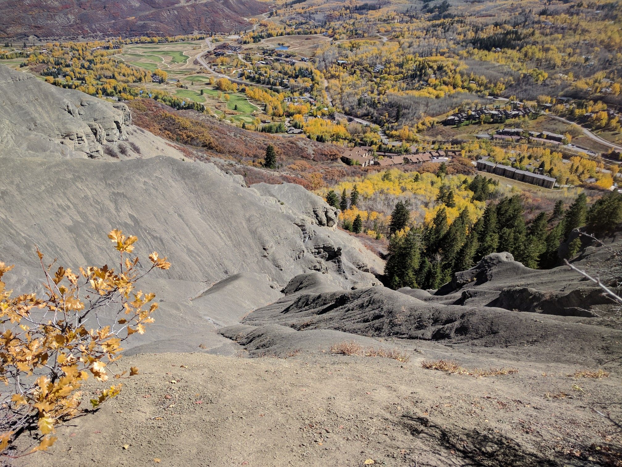 Steep, eroded hillside overlooks a valley with autumn trees and distant buildings. - Rim Trail loop