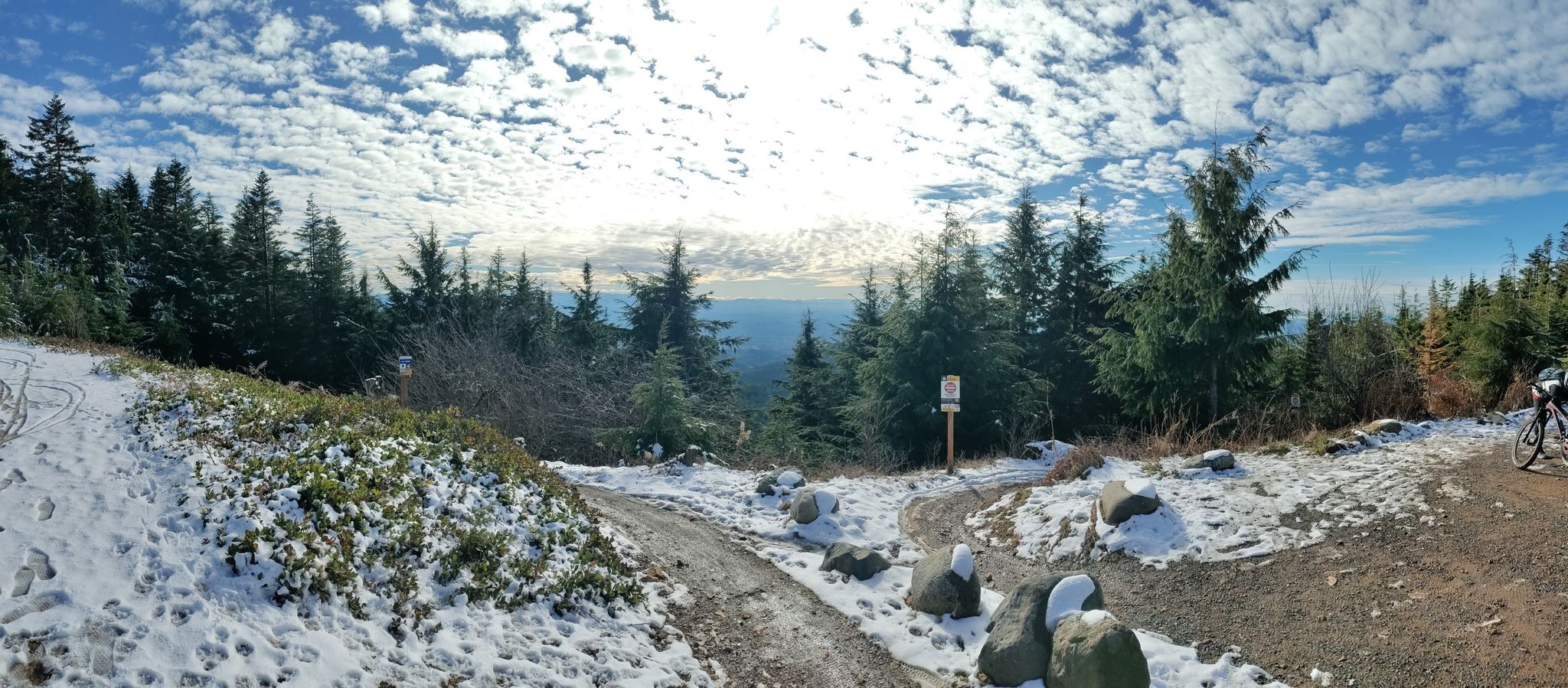 A snowy mountain trail intersection with pine trees under a bright, cloudy sky. - East Tiger Mountain Loop