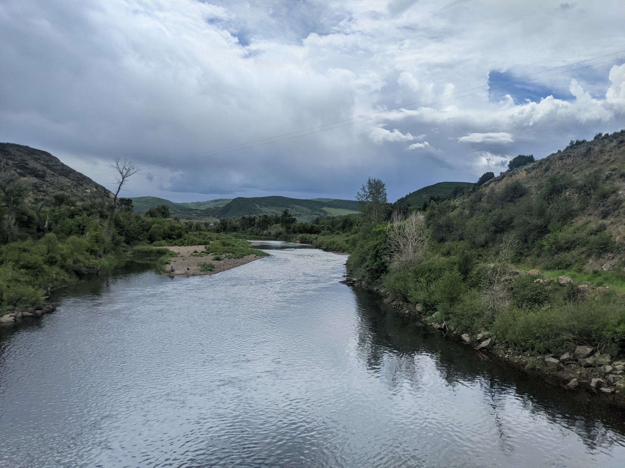 A wide river flows through green, tree-lined hills under a cloudy sky. - Hayden Loop