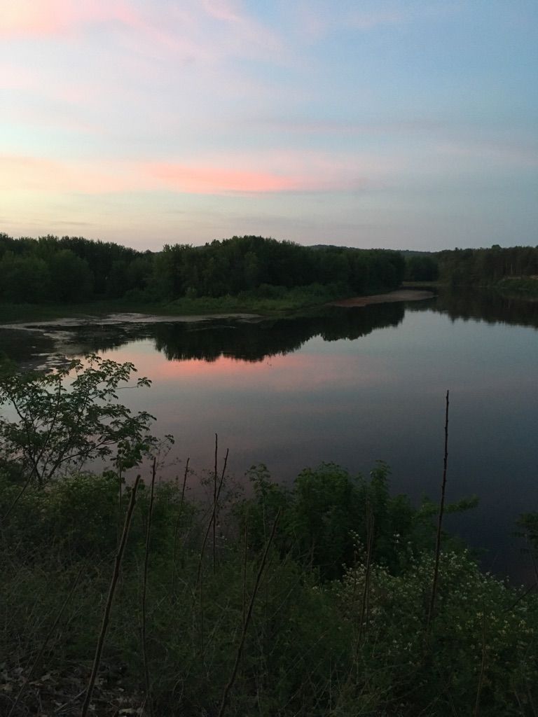River reflecting a vibrant pink and blue sunset sky, surrounded by dark trees. - Northern Rail Trail