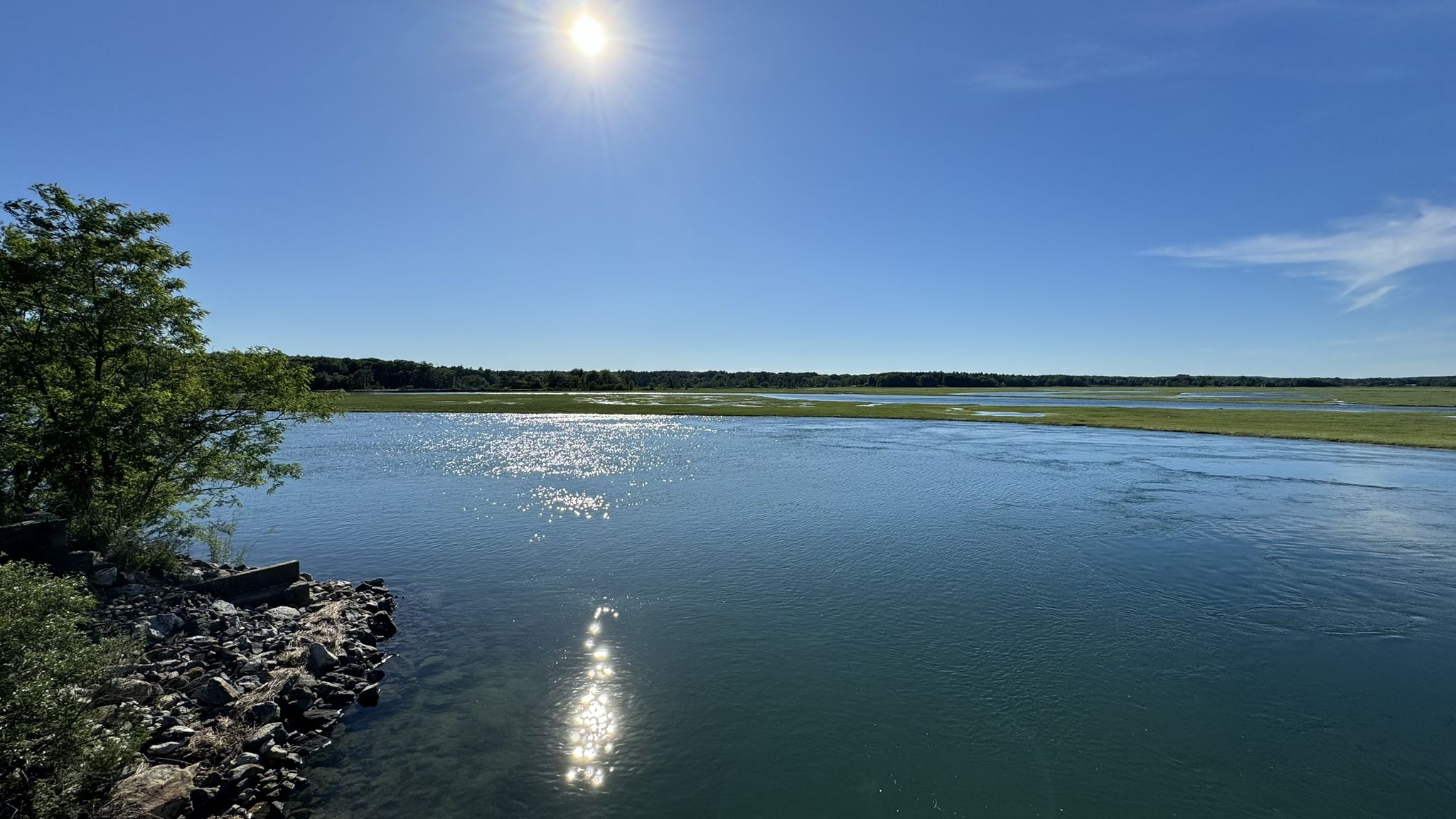 A wide river with sun reflecting brightly on the water and rocky banks. - Scarborough Marsh loop from Saco
