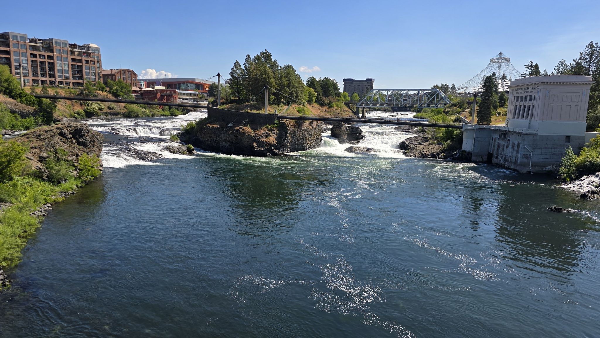 River with rapids, rocky islands, bridges, and buildings on a sunny day. - Bowl and Pitcher Overlook – Riverfront Park loop from Spokane
