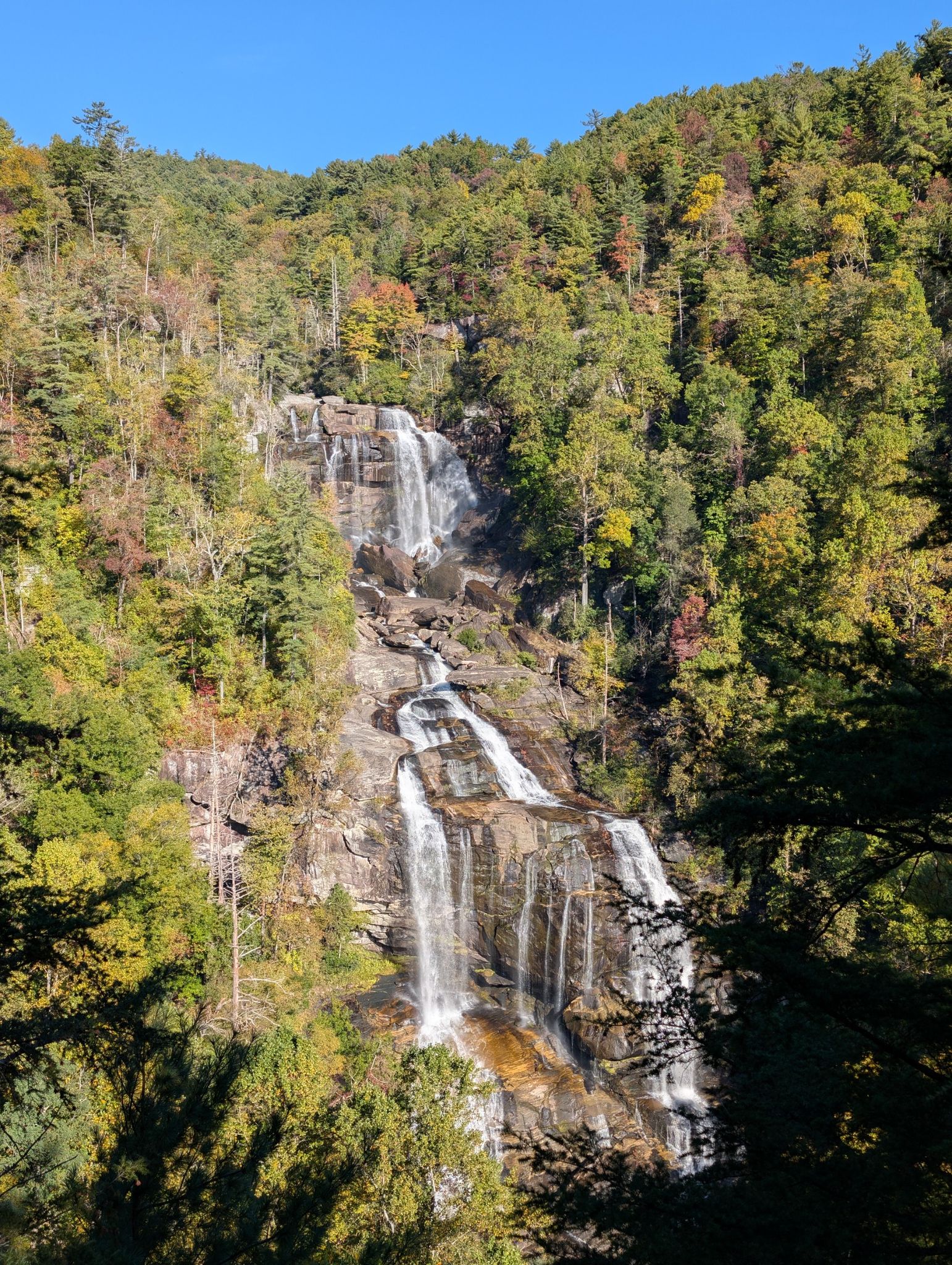 Multi-tiered waterfall flowing down a rocky mountain, surrounded by autumn trees. - Grassy Knob Loop
