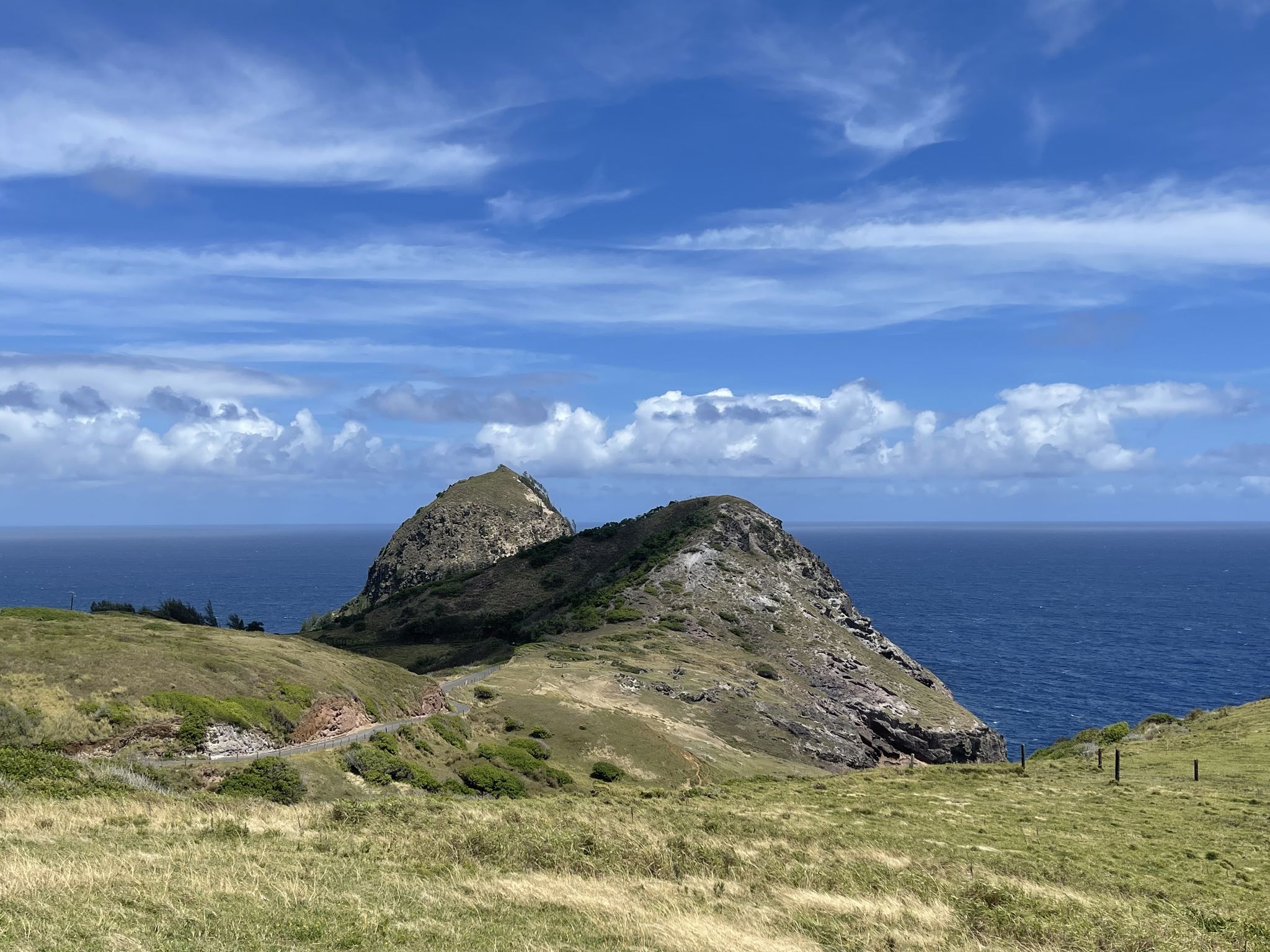 Green, rocky hills meet the vast blue ocean under a partly cloudy sky. - Mokulele Bike Path & Kahekili Highway loop
