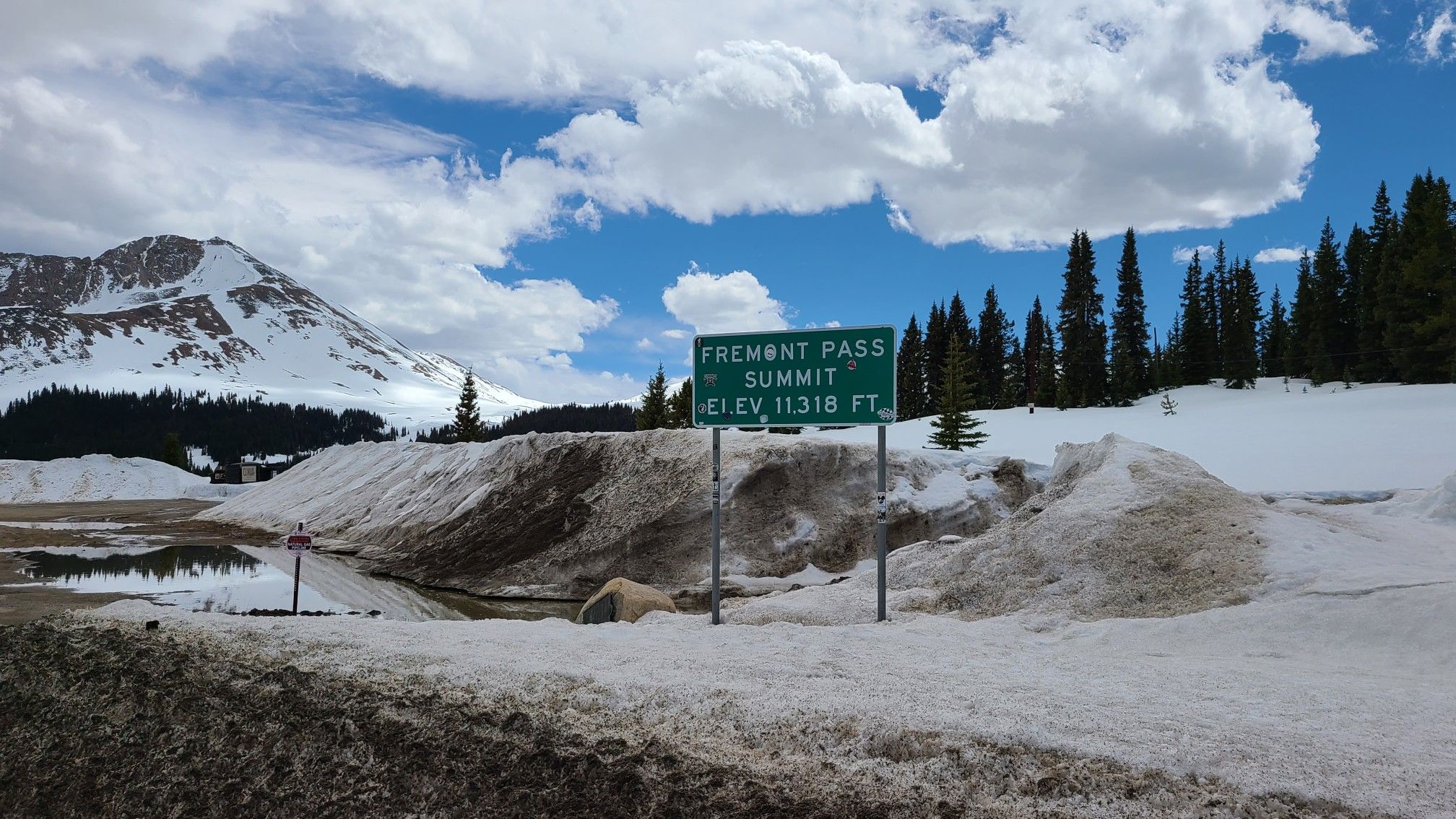 Road sign in deep snow with distant snow-capped mountains under a cloudy sky. - Fremont Pass Recreational Pathway